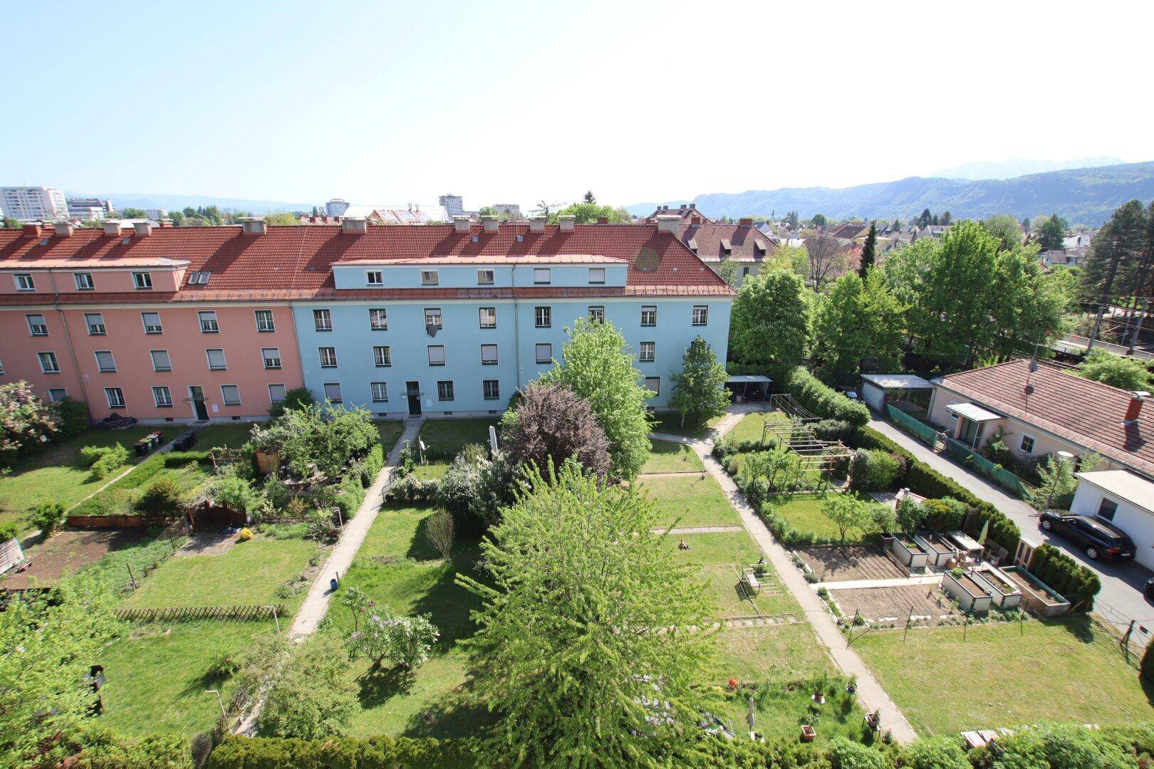Weitläufiger Blick auf grüne Gärten und umliegende Wohngebäude unter klarem Himmel.