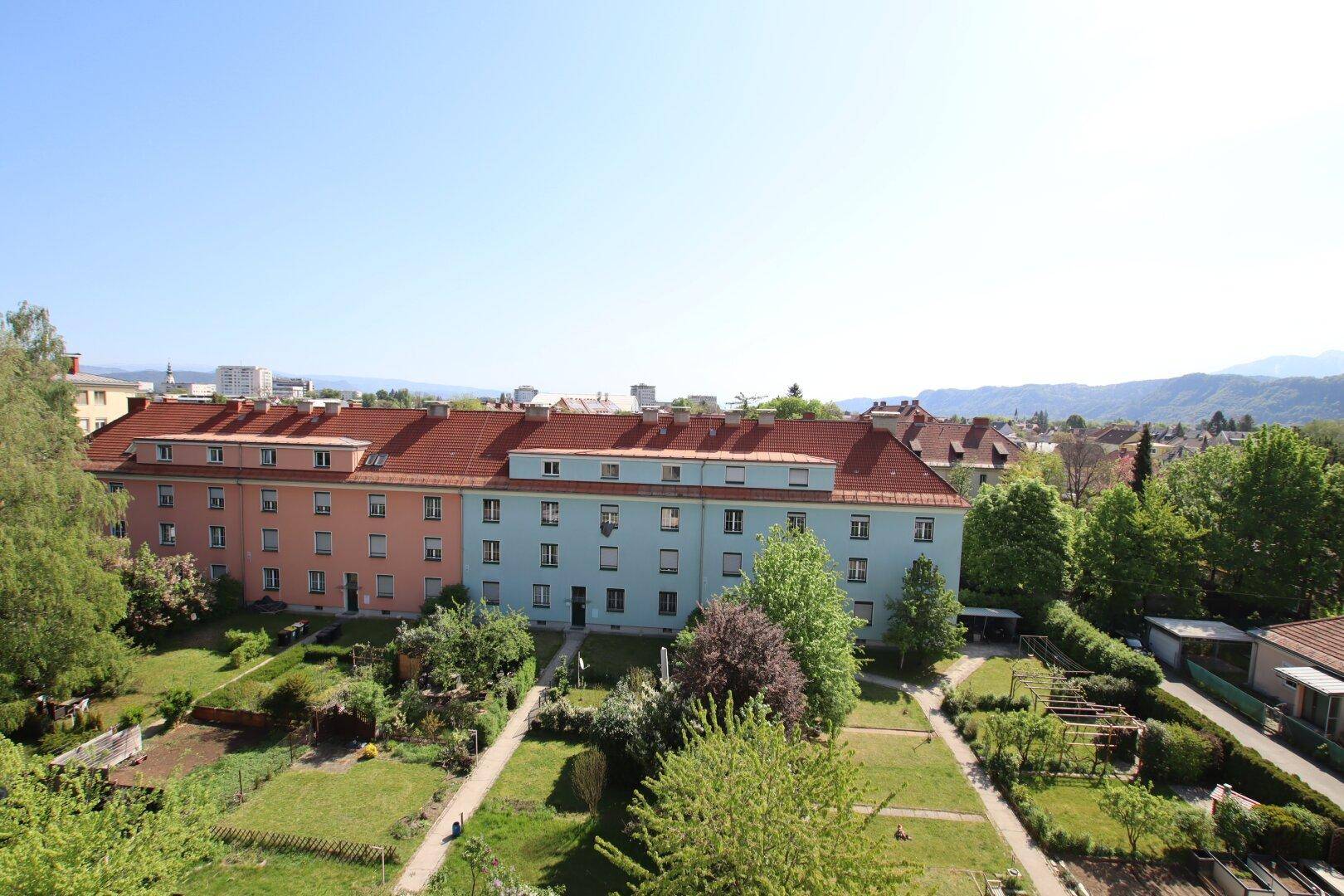 Panoramablick über gepflegte Gärten und benachbarte Wohnblöcke an einem sonnigen Tag.