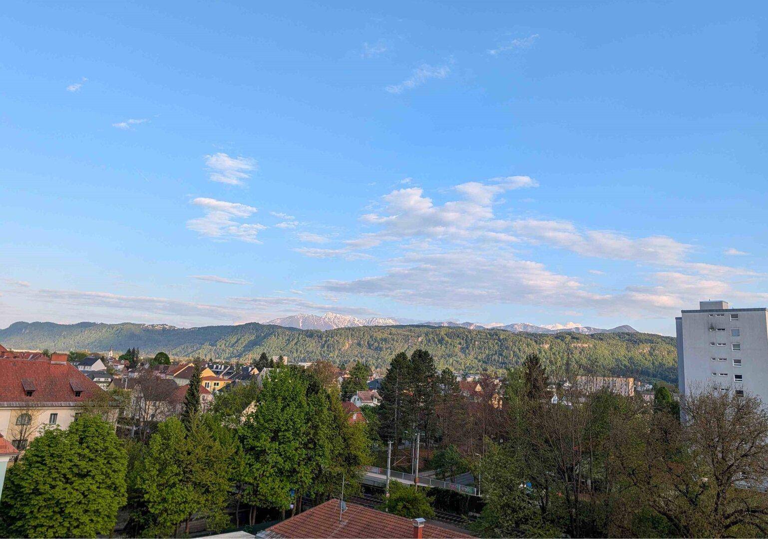 Malerischer Ausblick auf die Stadt und schneebedeckte Berge am Horizont unter blauem Himmel.