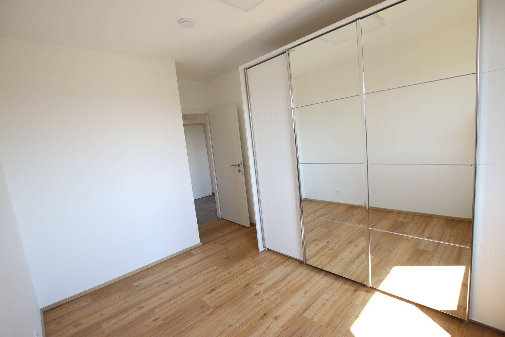 Schlafzimmer mit hellem Laminatboden und großem Spiegelschrank, der den Raum optisch vergrößert.