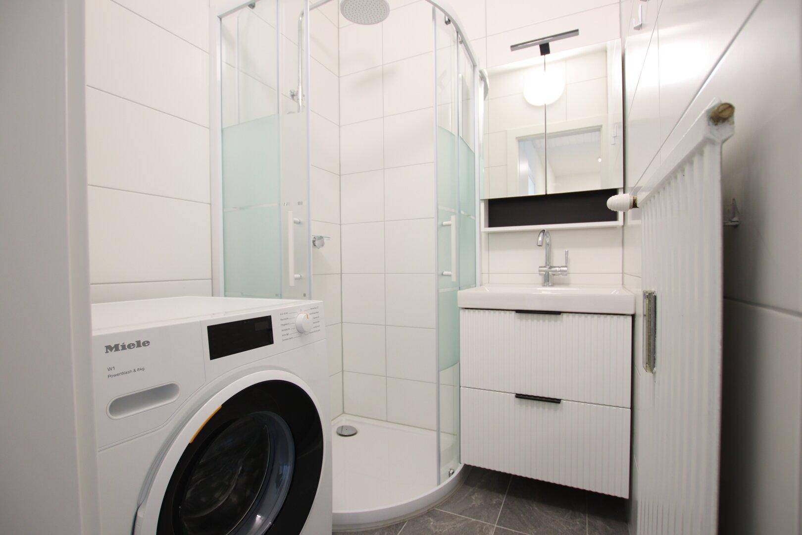 Modernes Badezimmer mit Duschkabine, Waschbeckenunterschrank und Waschmaschine.