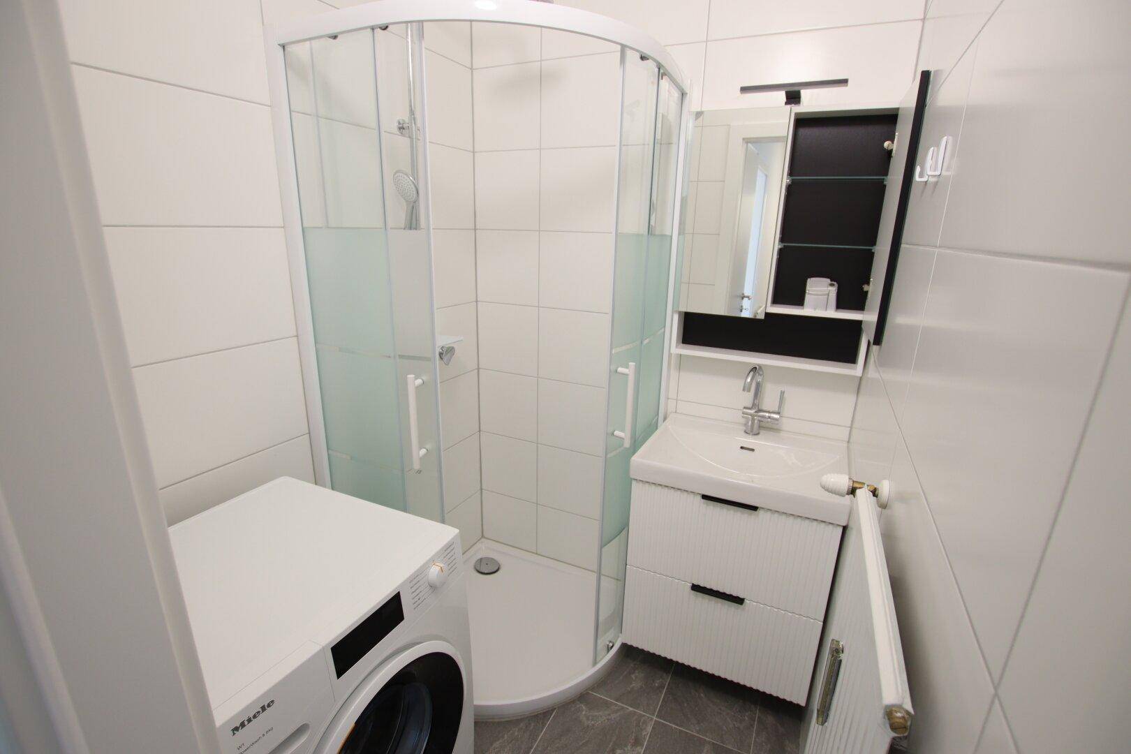 Helles Badezimmer mit weiß gefliesten Wänden, Duschkabine und modernem Waschtisch.