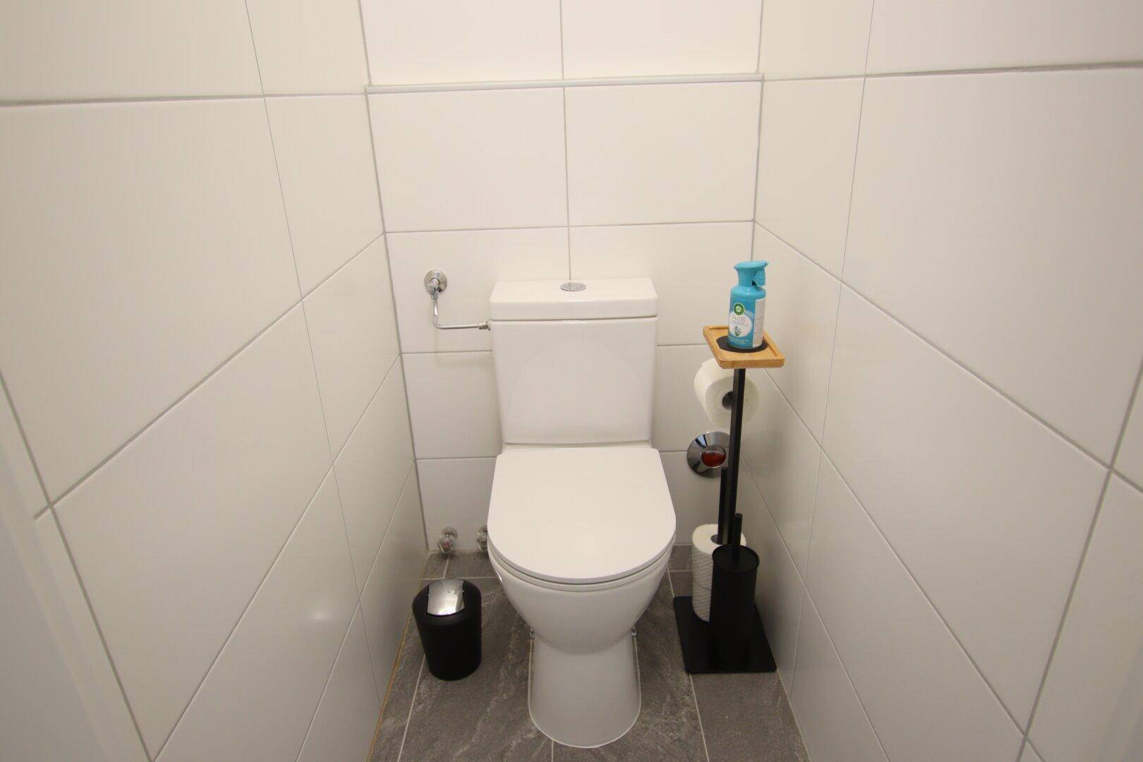 Separates WC mit weißer Toilette und Fliesen an Wänden und Boden.