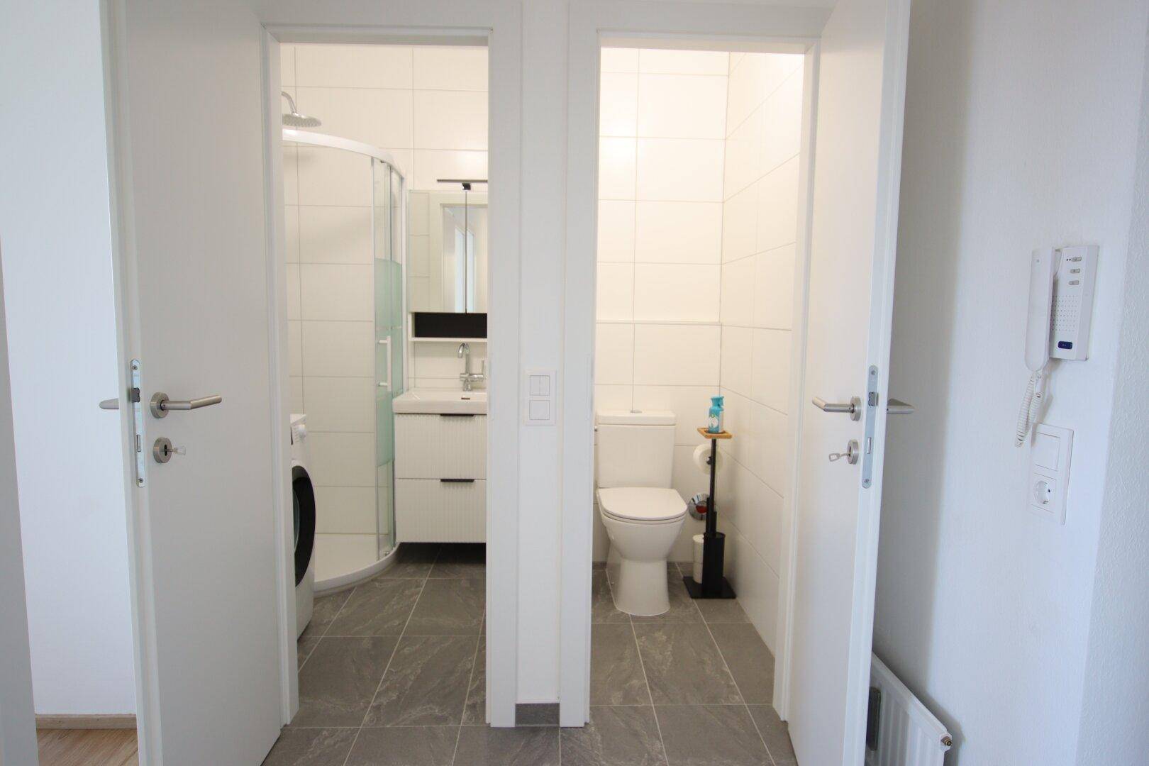 Flur mit Zugang zu einem Badezimmer und einem separaten WC, beide mit Fliesenboden.