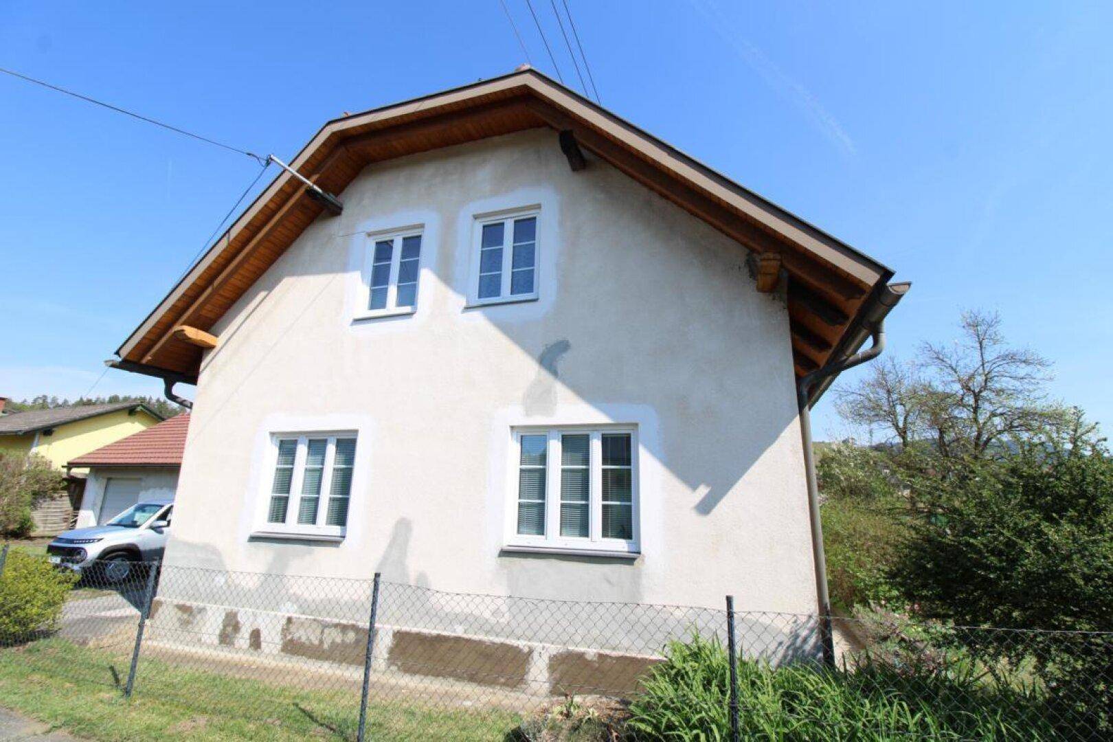 Seitenansicht des Hauses mit sichtbarer Holzkonstruktion unter dem Dach und weißen Fenstern.