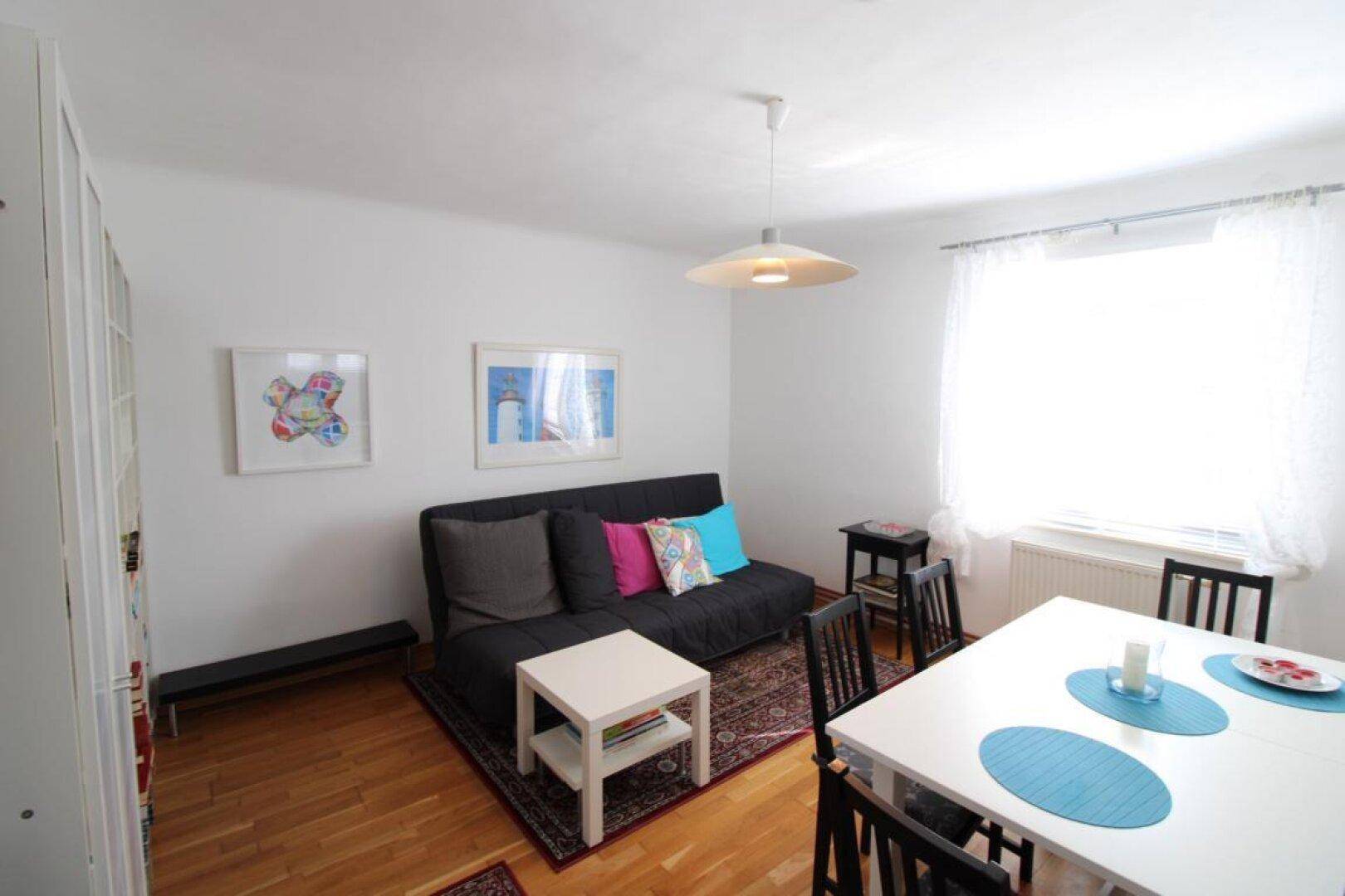 Heller Wohn- und Essbereich mit Holzboden, Sofa und Esstisch, modern dekoriert.
