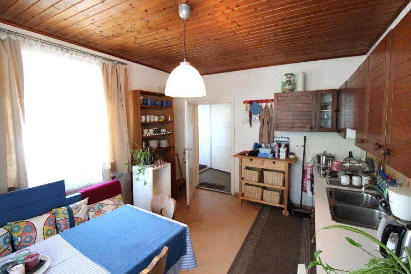 Gemütliche Küche mit Holzbalkendecke, Essbereich und Blick nach draußen durch ein Fenster.