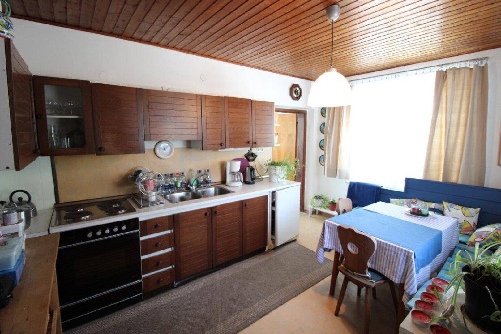 Funktionale Küche mit Holzschränken, Spüle und Herd, integriertem Essbereich und Kühlschrank.