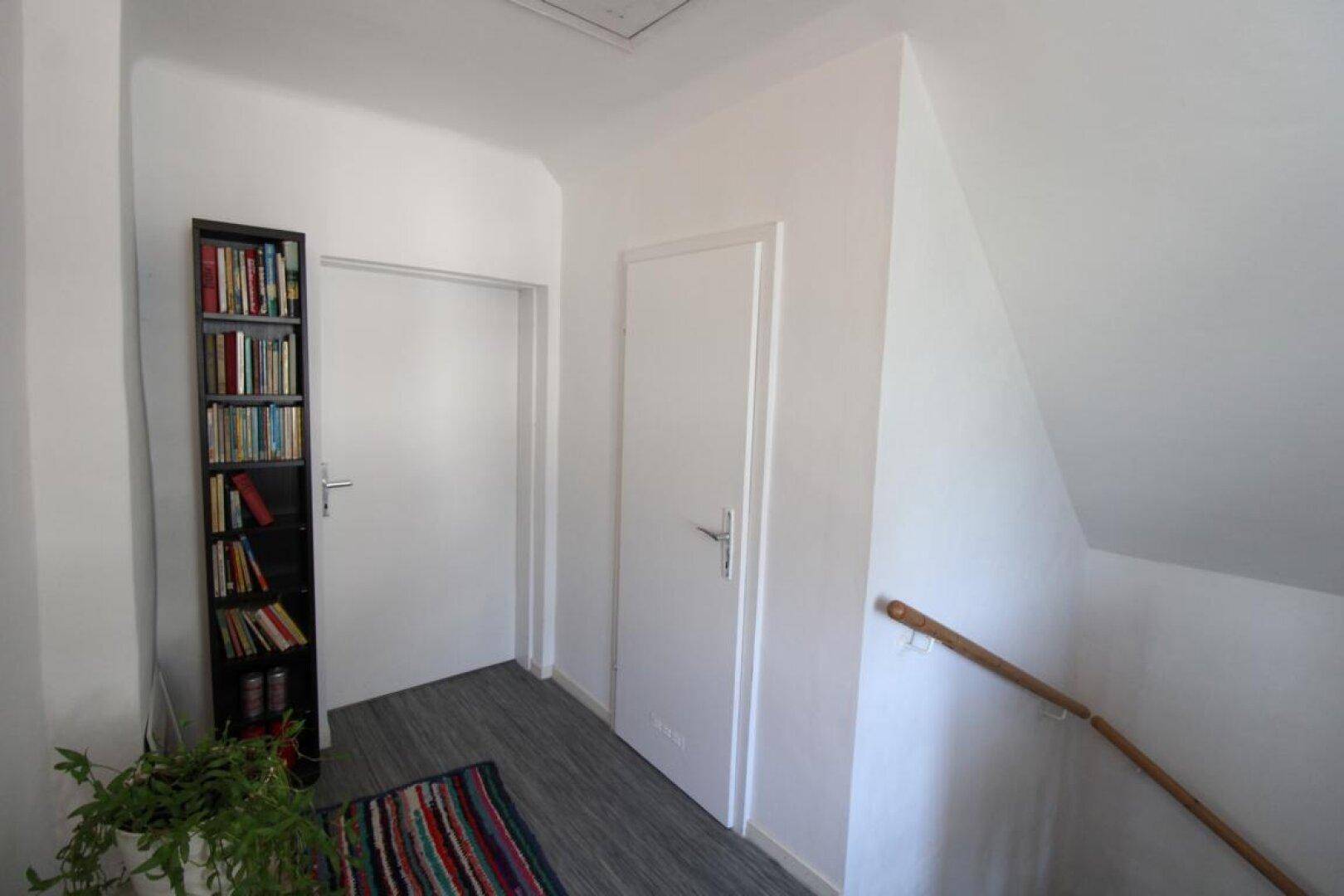 Heller Flur im Dachgeschoss mit Bücherregal und Zugang zu weiteren Räumen.