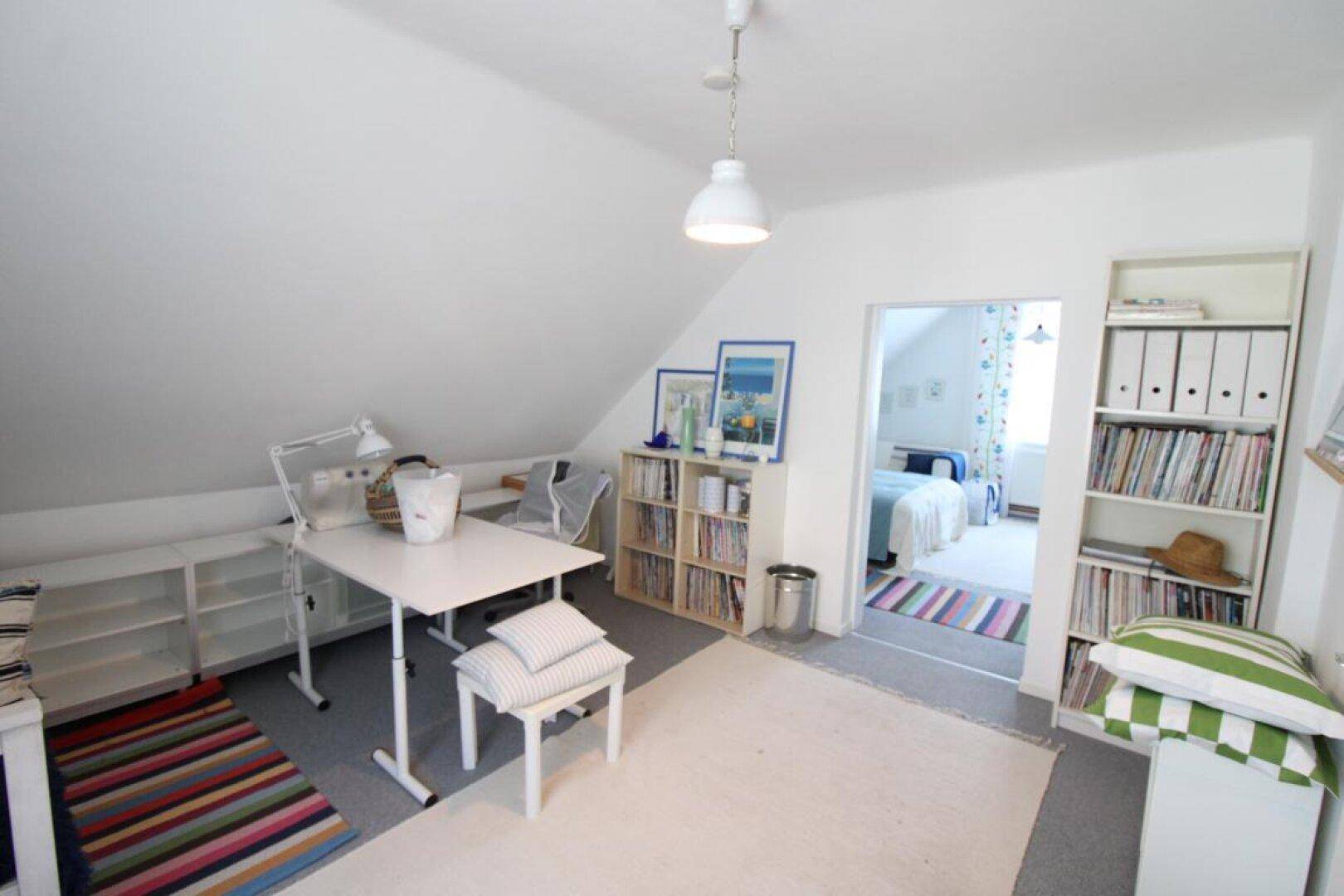 Geräumiges Dachzimmer als Arbeitsbereich mit Schreibtisch und Blick in ein angrenzendes Schlafzimmer.