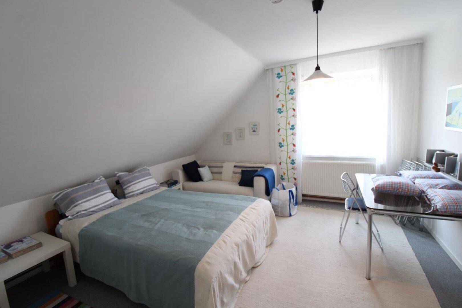Gemütliches Schlafzimmer im Dachgeschoss mit Doppelbett, Sofa und viel Tageslicht.