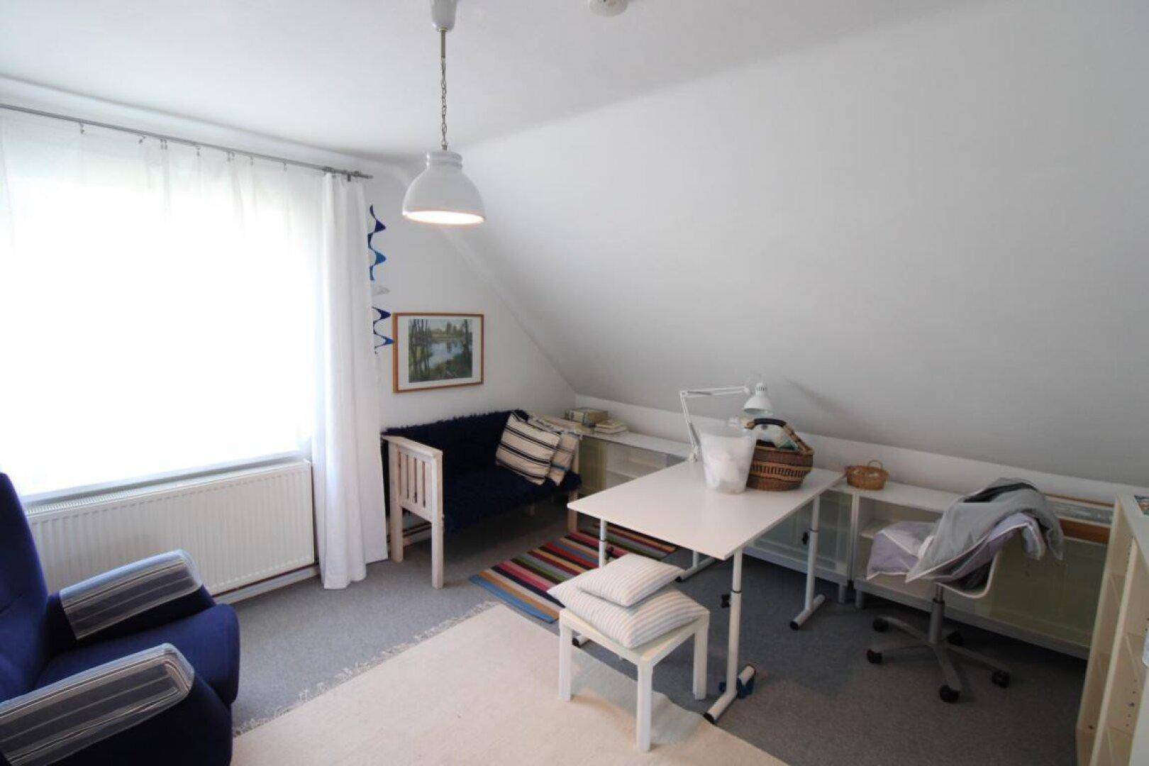 Helles Dachzimmer mit Arbeitsbereich, bequemen Sitzgelegenheiten und schrägen Wänden.