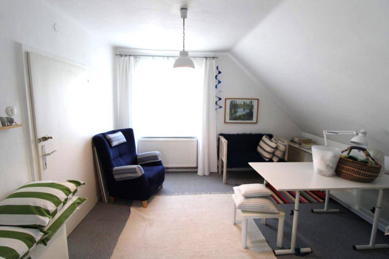 Vielseitiges Dachzimmer mit Arbeitsplatz, Lesesessel und Stauraum unter der Dachschräge.