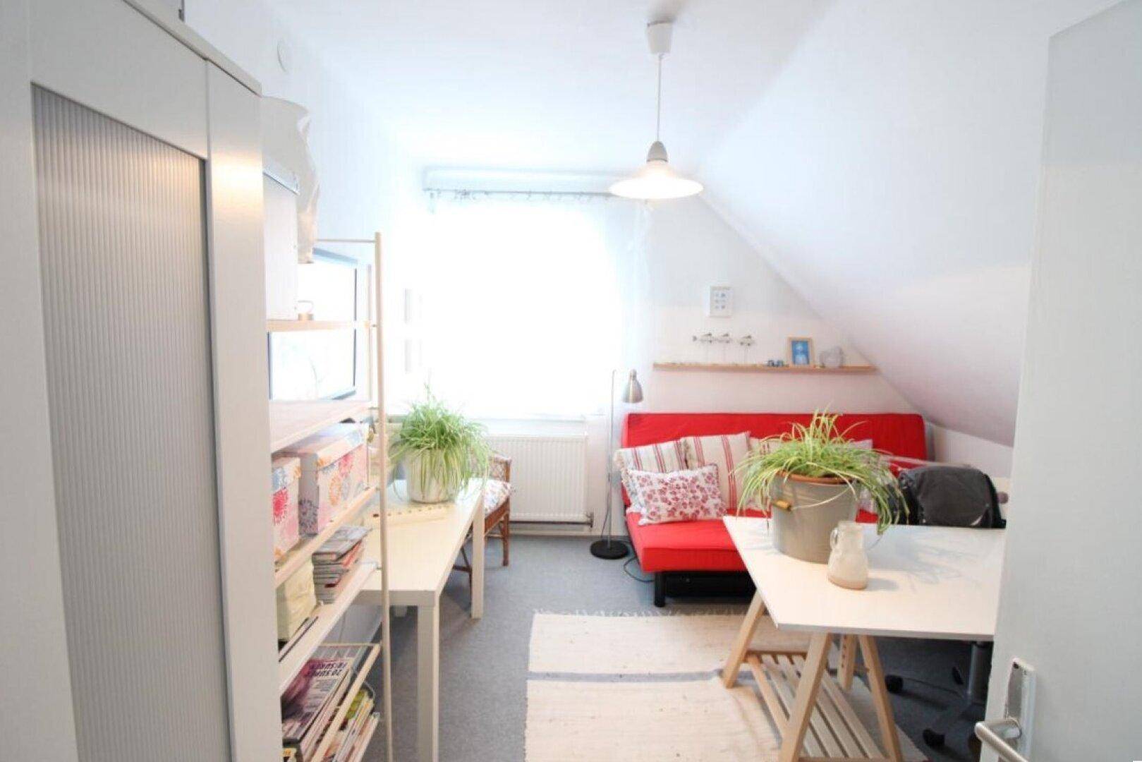 Helles Dachzimmer als Arbeits- oder Gästezimmer mit rotem Sofa und Schreibtisch.