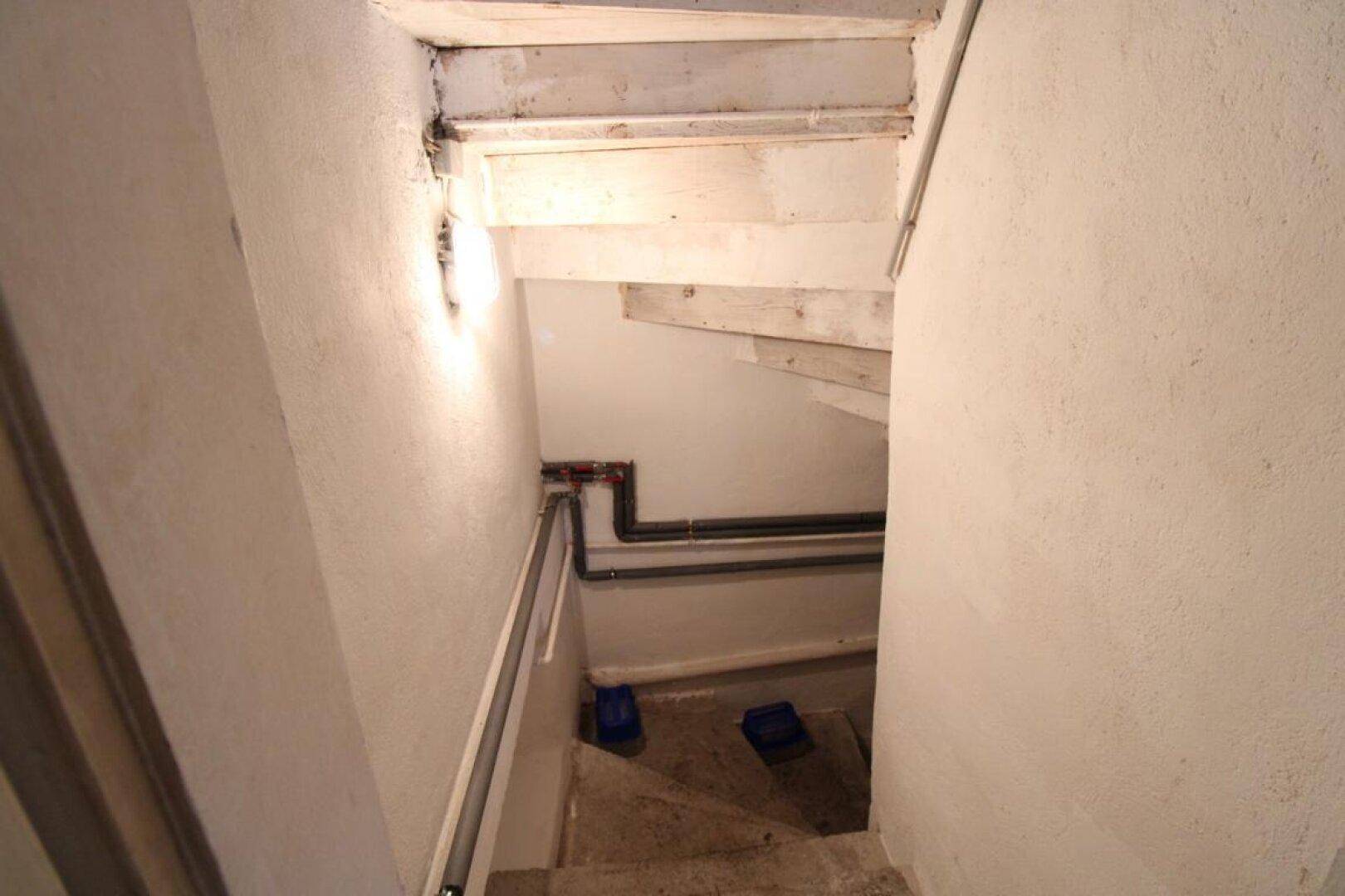 Kellerabgang mit rohen Betonstufen und freiliegenden Versorgungsleitungen.