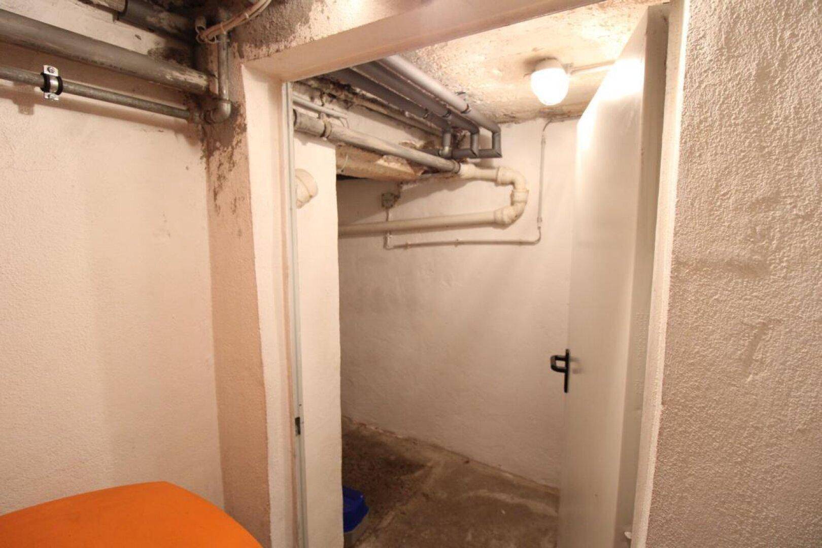 Kleiner Kellerraum mit einfacher Ausstattung und sichtbaren Deckenrohren.
