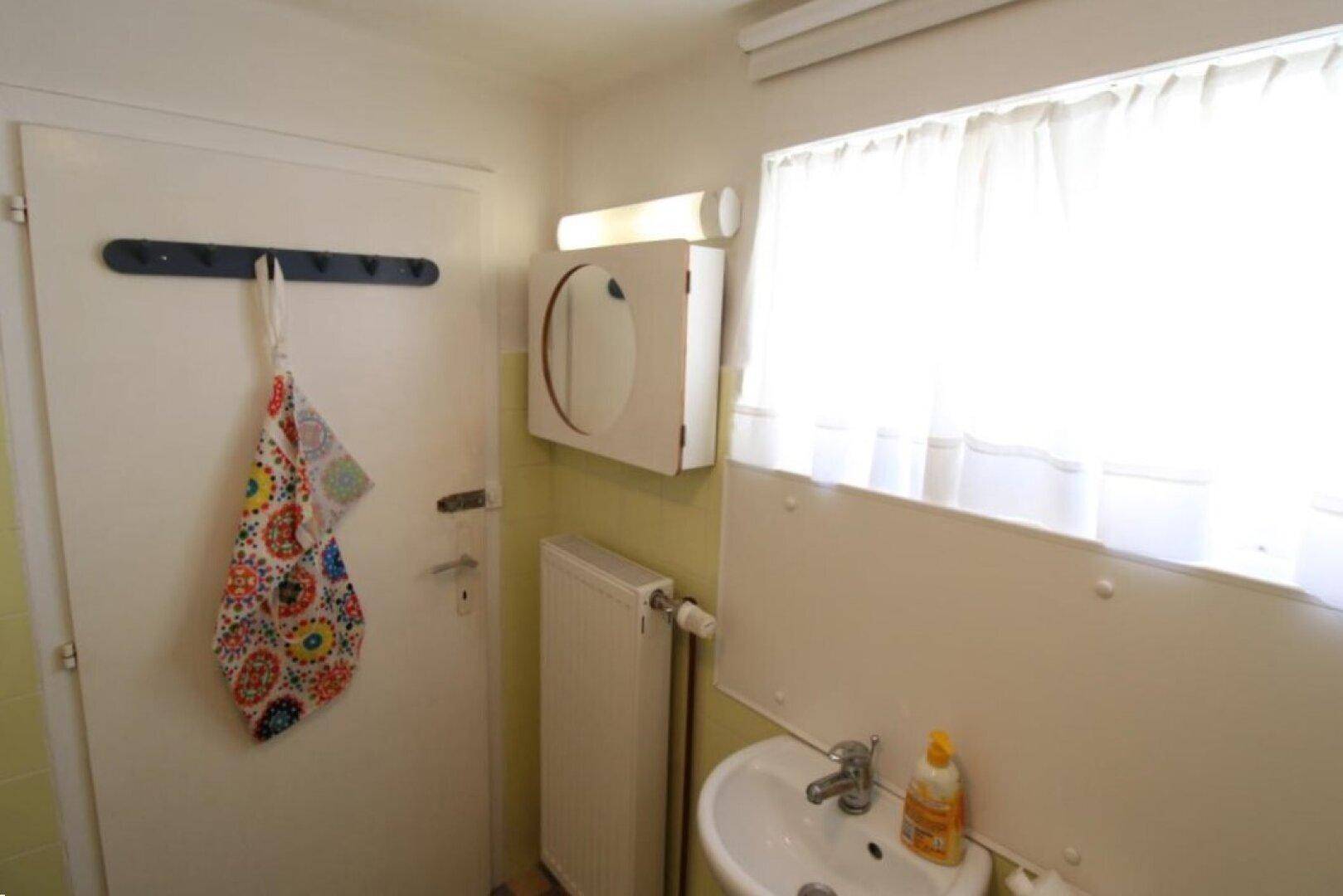 Badezimmer mit Waschbecken, Spiegelschrank und Fenster, helle und funktionale Einrichtung.