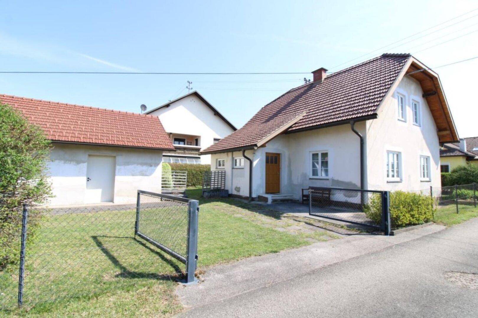 Ansicht des Hauses und der Garage von der Straße aus, mit einem Zaun und Rasenfläche.