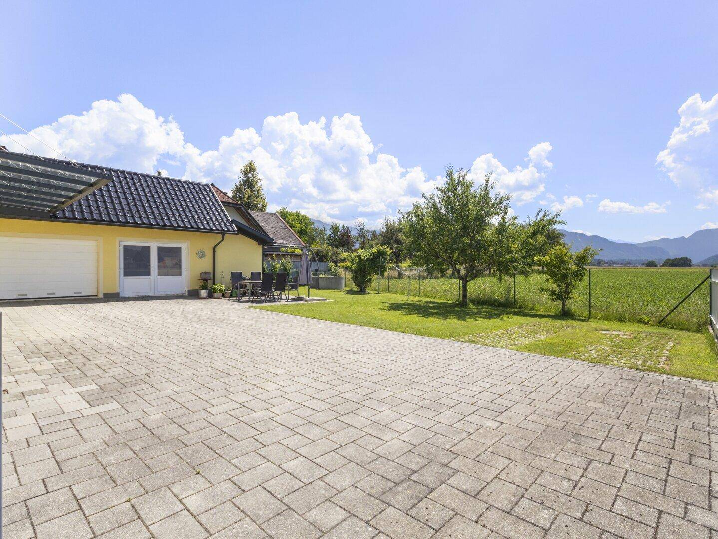 Große gepflasterte Auffahrt neben dem Garten mit Obstbäumen und Bergblick.