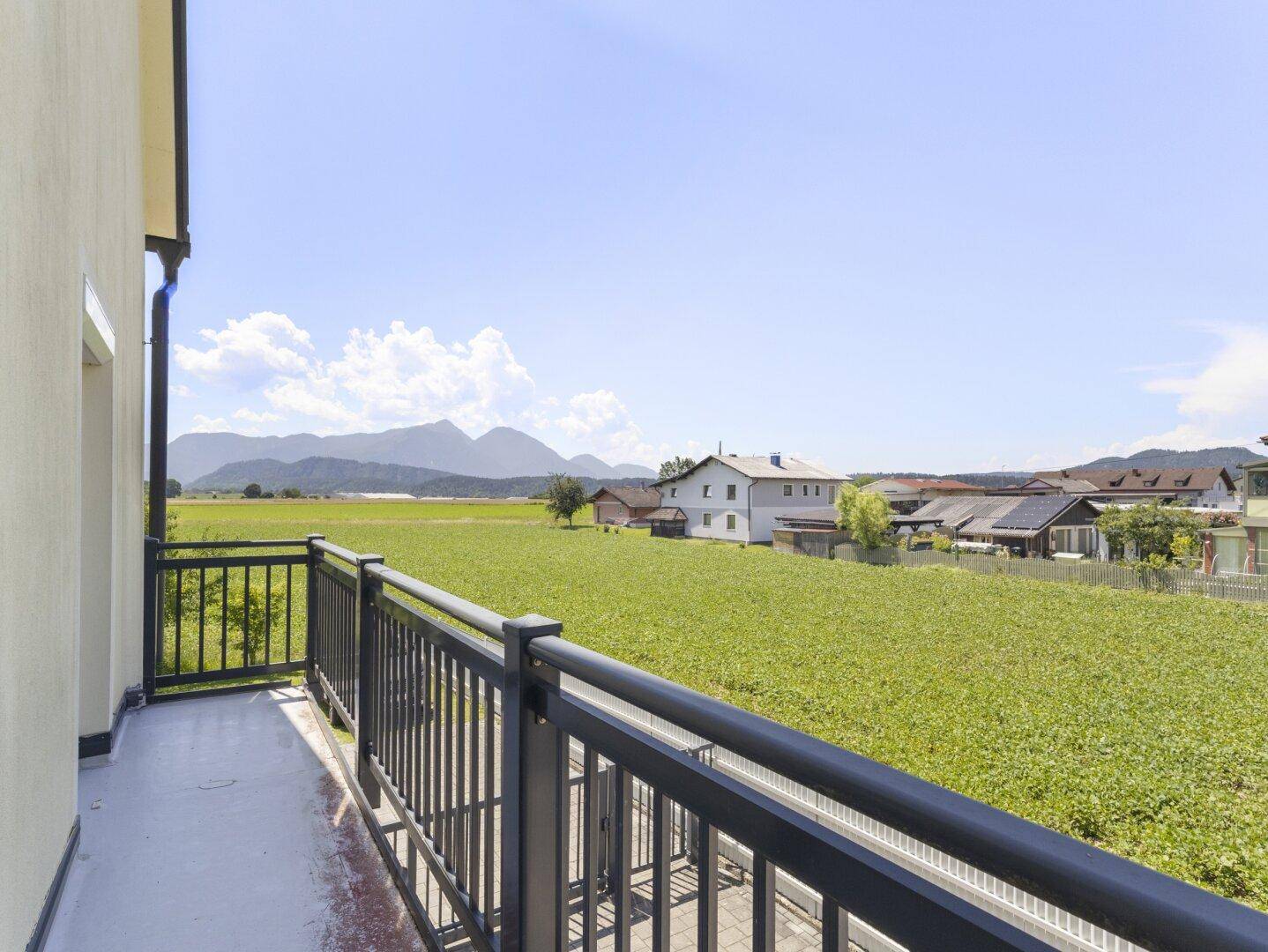 Balkon mit schwarzem Geländer bietet einen weiten Blick über grüne Felder und Berge.