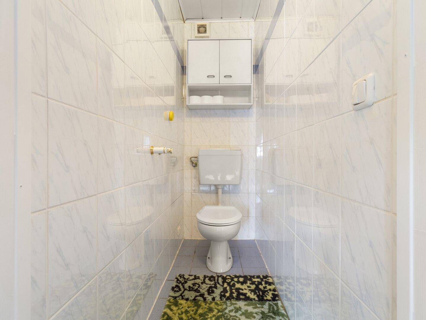 Kleines WC mit weißen Fliesen, Wand-WC und praktischem Spiegelschrank.