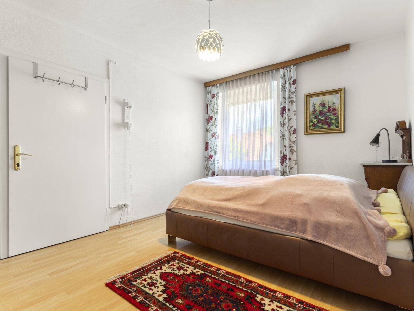 Gemütliches Schlafzimmer mit Holzboden, Doppelbett und Fenster mit Vorhängen.