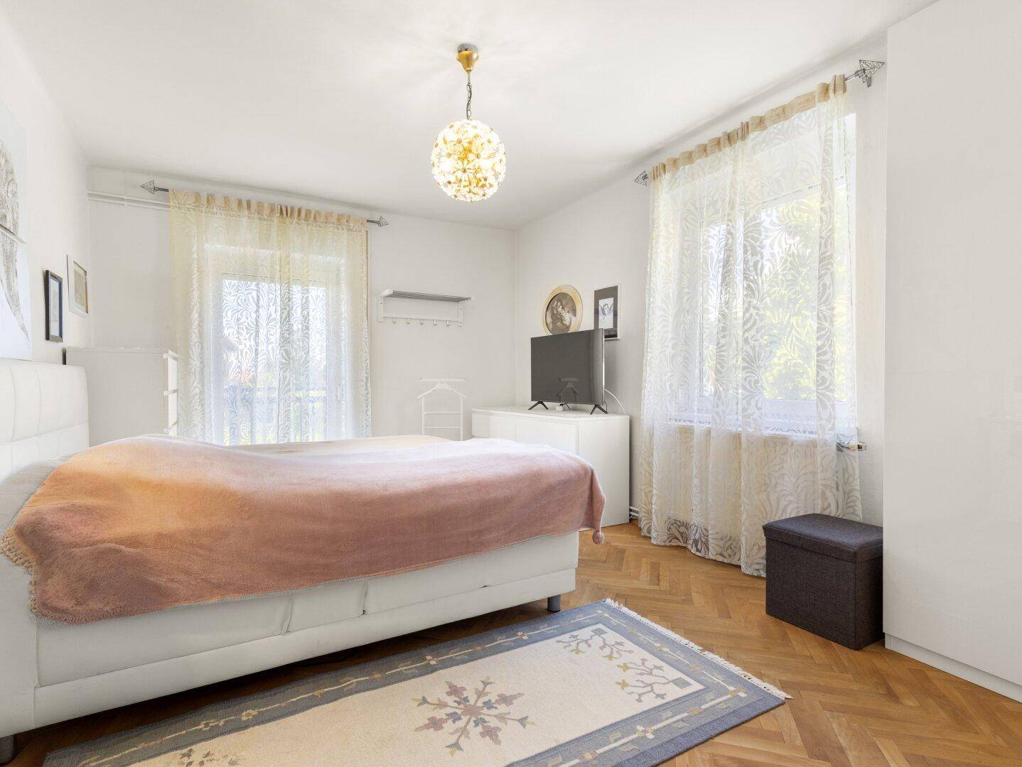 Helles Schlafzimmer mit Parkettboden, Doppelbett und großem Fenster für viel Tageslicht.