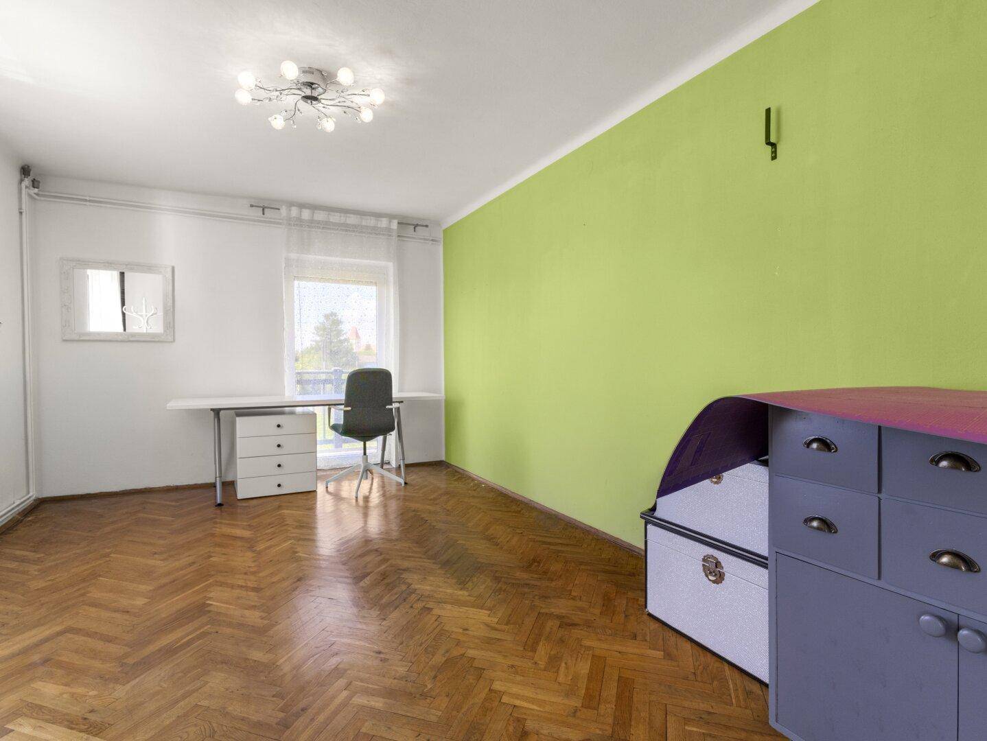 Helles Arbeitszimmer mit Parkettboden, Schreibtisch und einer auffälligen grünen Wand.