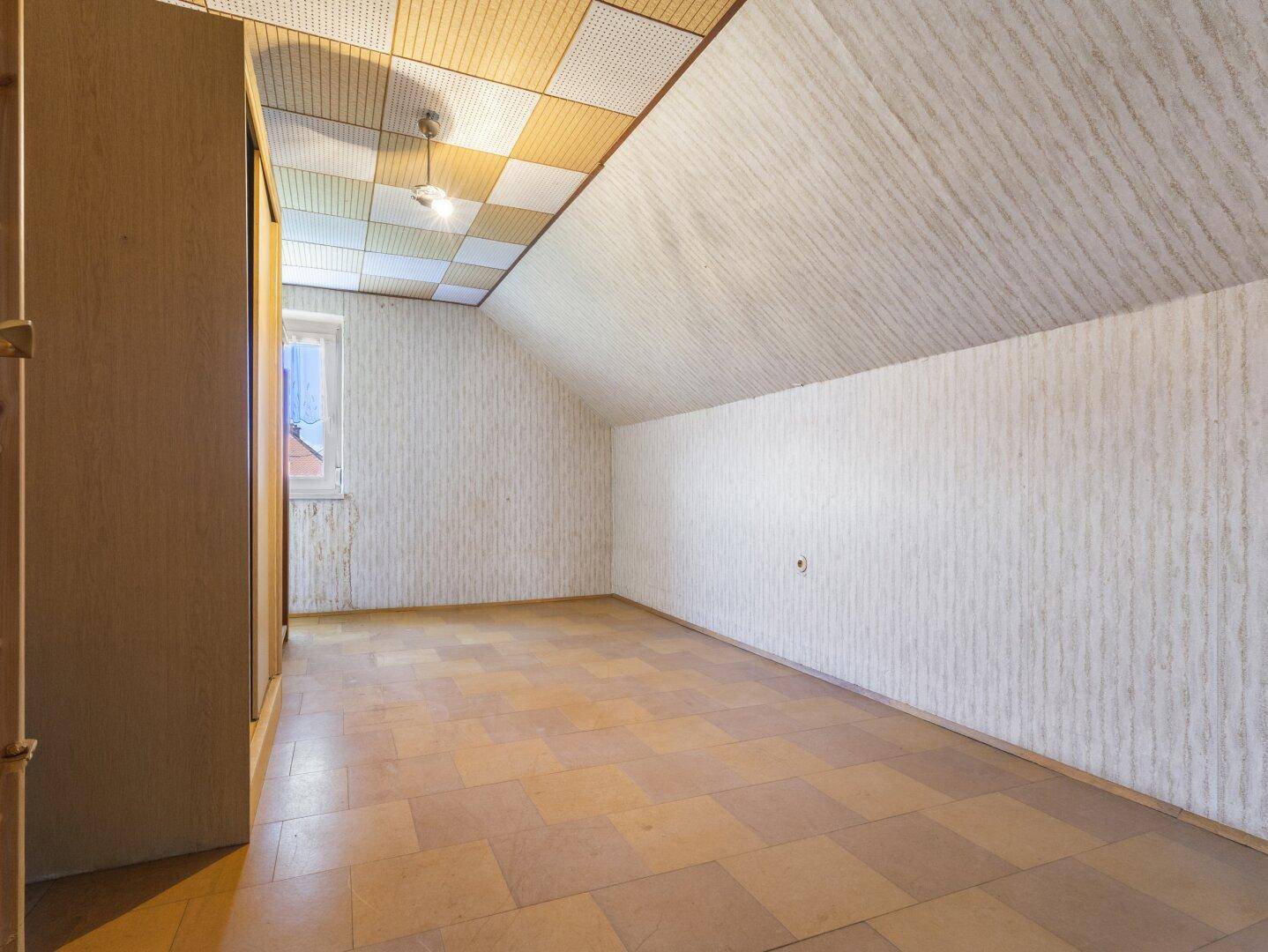 Geräumiger Dachbodenraum mit schräger Decke, Fenster und einfacher Ausstattung.