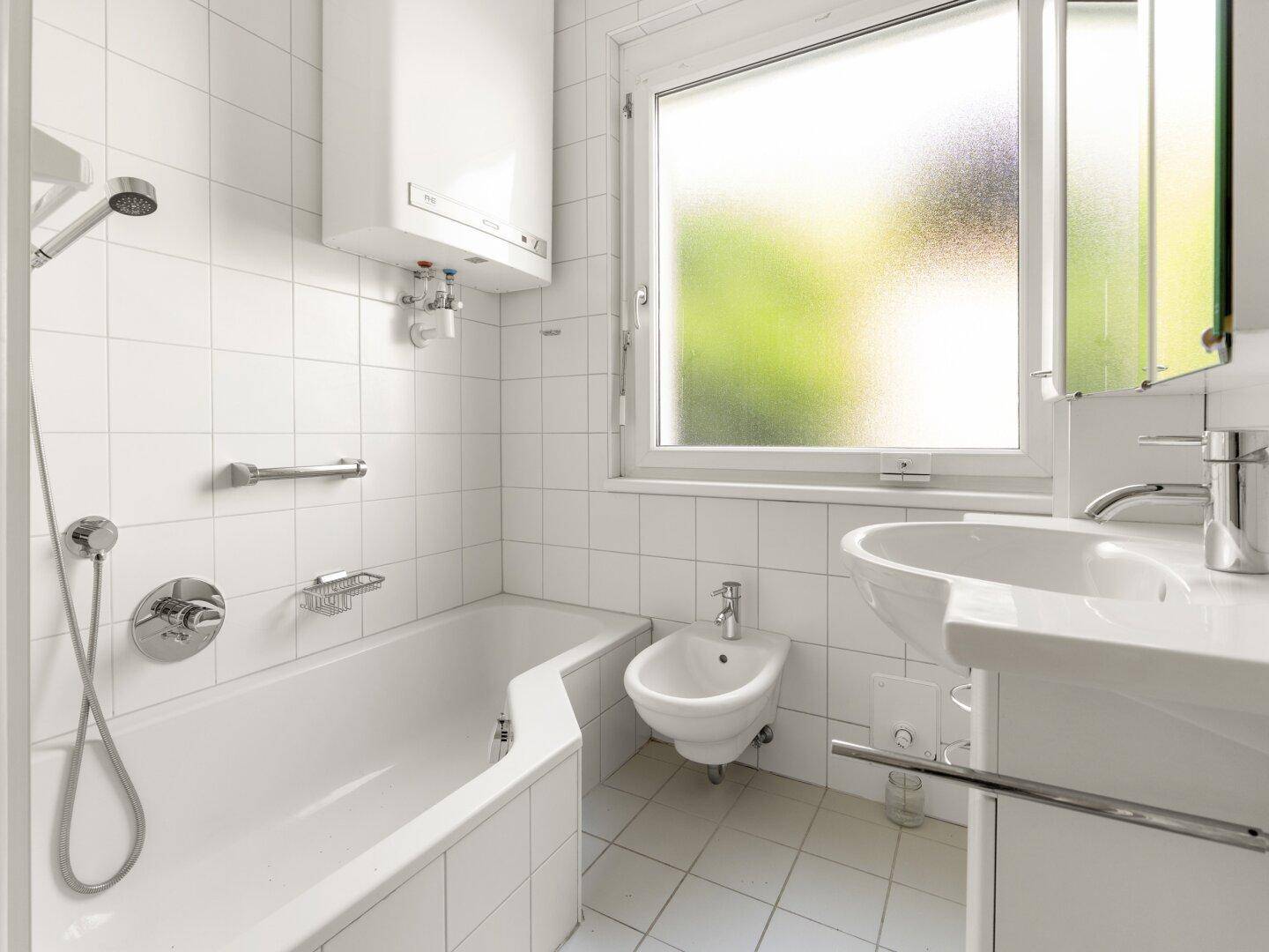 Gefliestes Badezimmer mit Badewanne, Dusche, Waschbecken, Bidet und einem Fenster.
