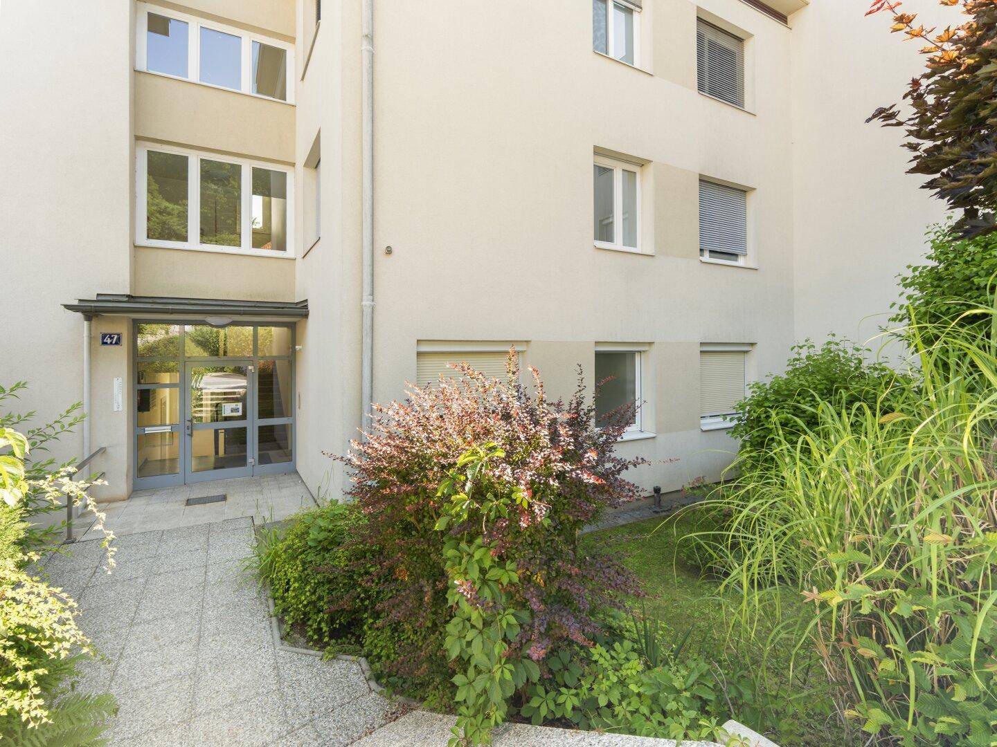 Haupteingang des Gebäudes mit gepflegter Bepflanzung und einem Gehweg.