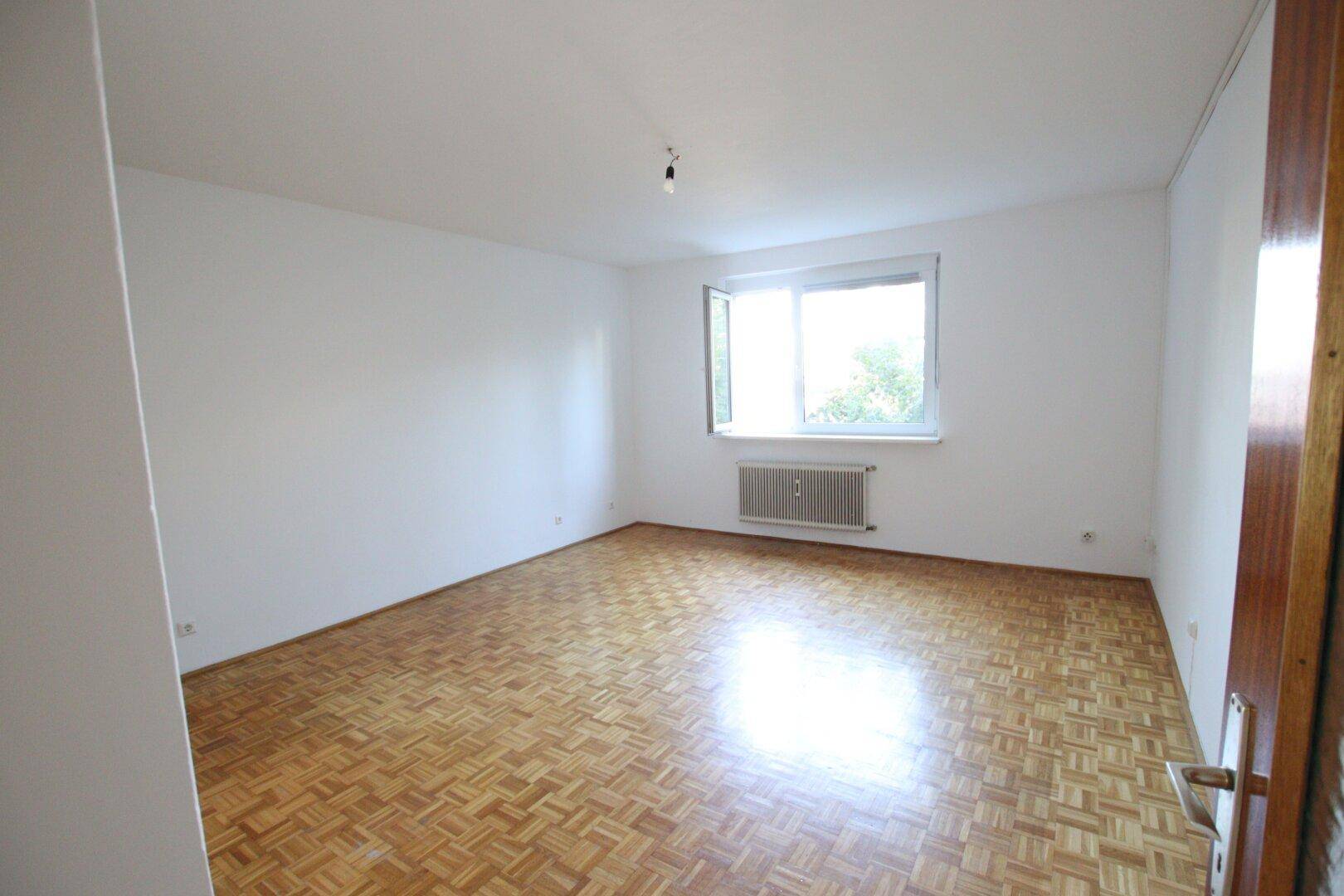Helles Schlafzimmer mit Parkettboden und Fenster, bietet eine ruhige und gemütliche Atmosphäre.