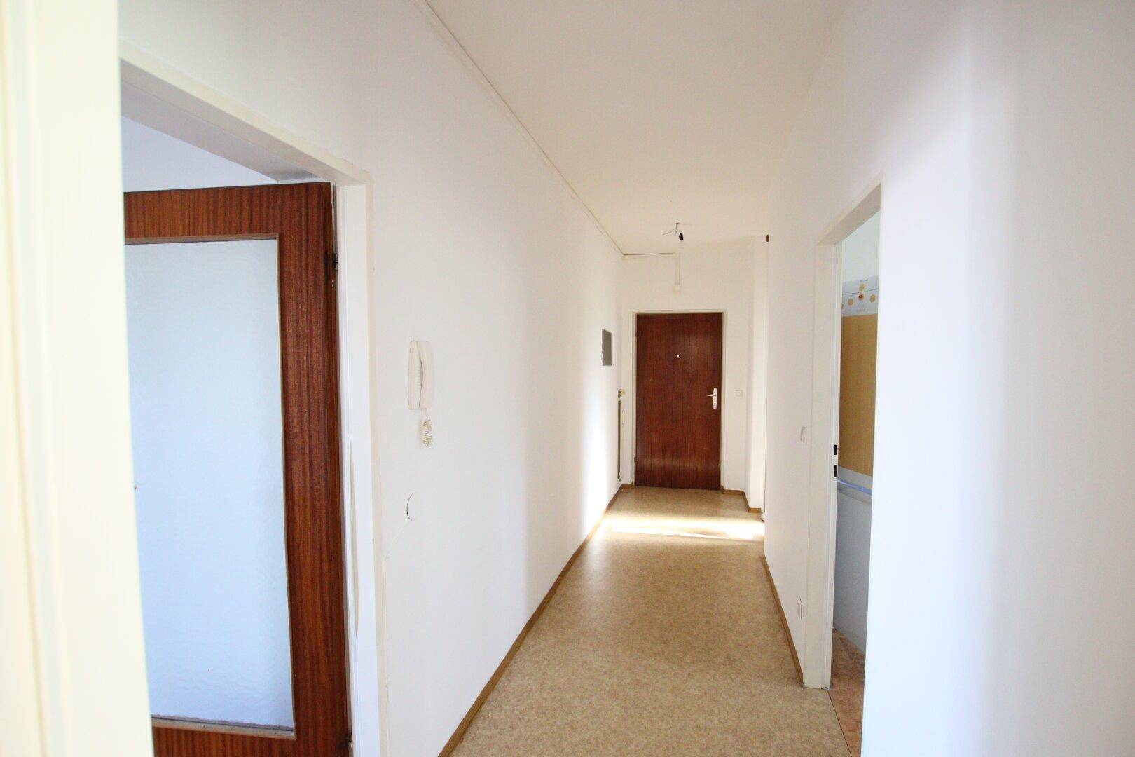 Langer Flur mit Linoleumboden und Holztüren, verbindet die verschiedenen Räume der Wohnung.