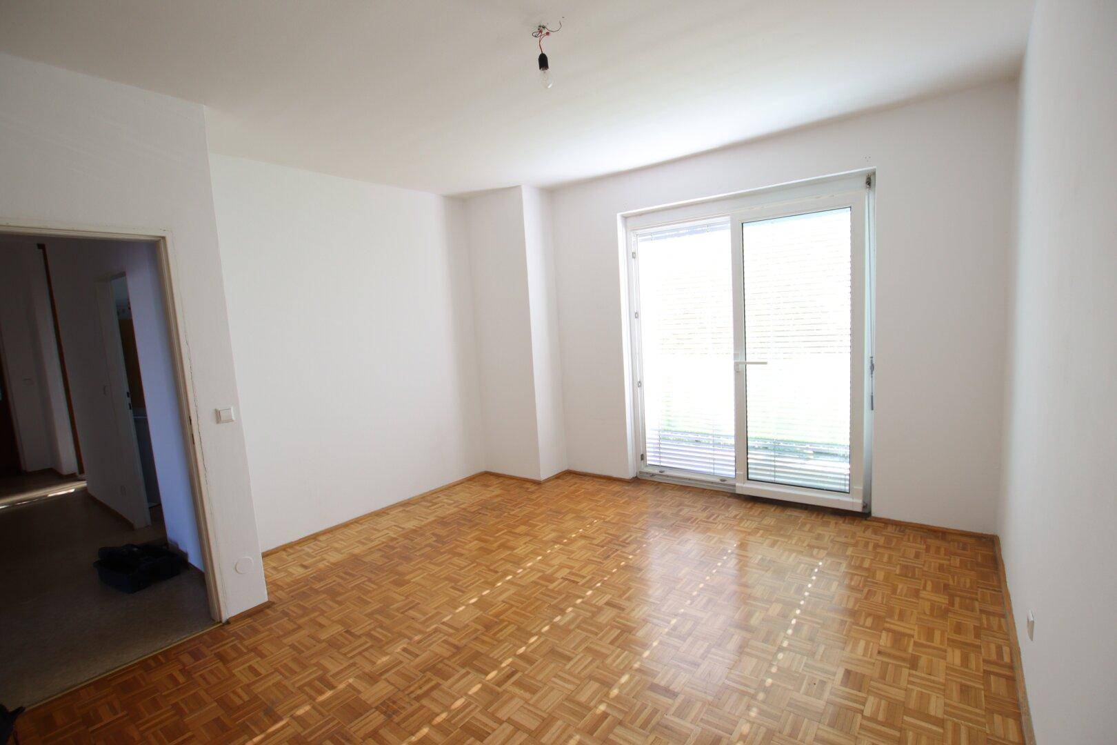 Geräumiges Zimmer mit Parkettboden und großem Fenster, bietet viel Tageslicht und eine angenehme Atmosphäre.