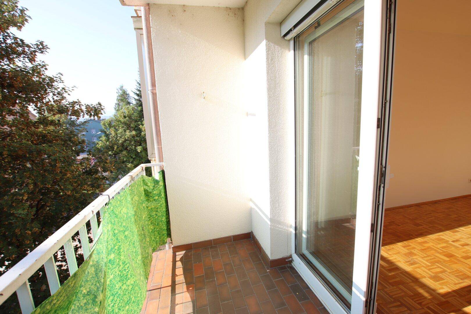 Kleiner Balkon mit Fliesenboden und Blick ins Grüne, ideal zum Entspannen im Freien.