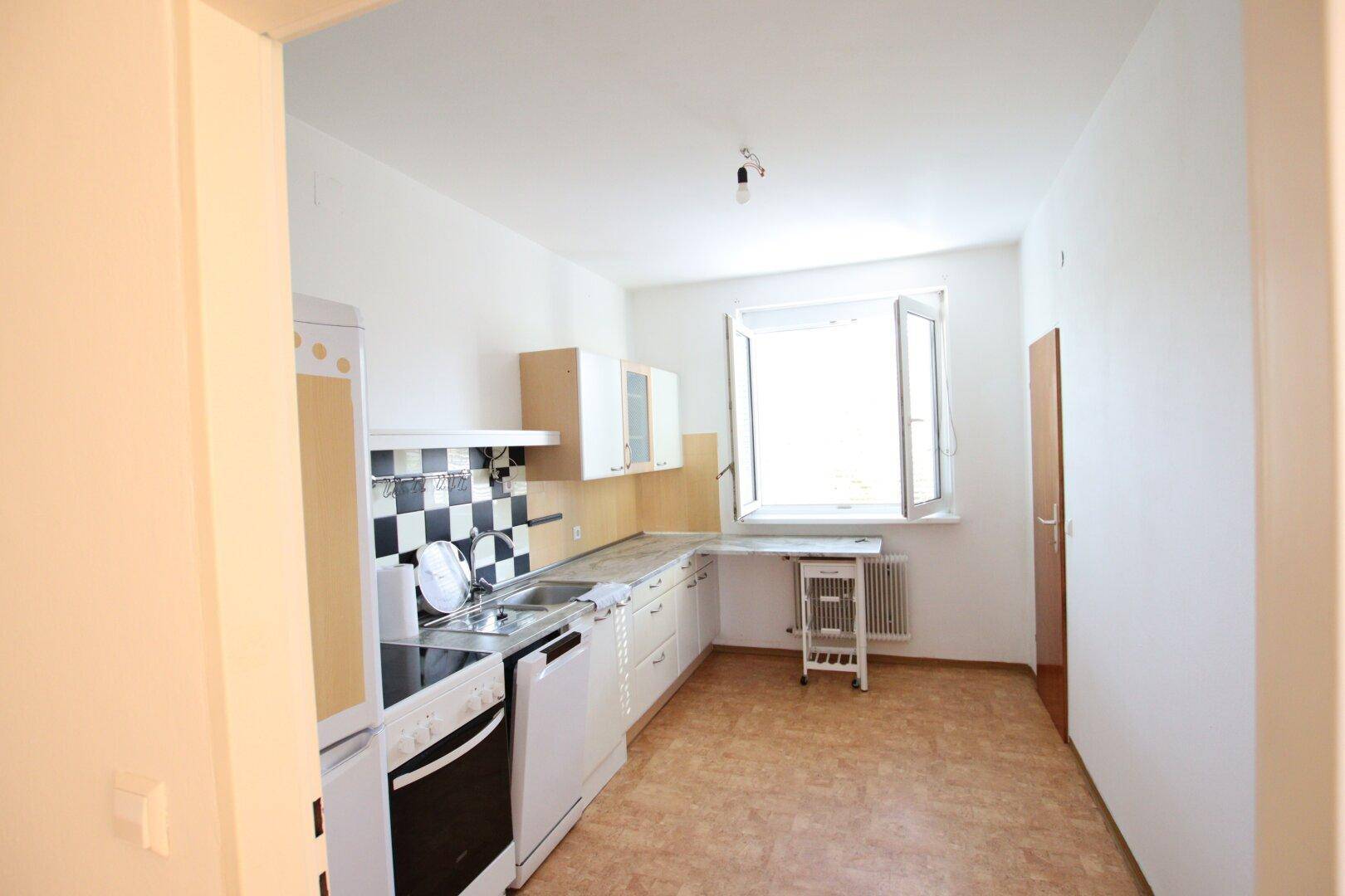 Funktionale Küche mit Fenster und Linoleumboden, ausgestattet mit grundlegenden Geräten und Stauraum.