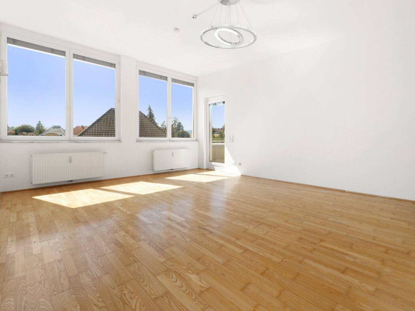 Lichtdurchflutetes Wohnzimmer mit großen Fenstern und einem angenehmen Blick ins Grüne.