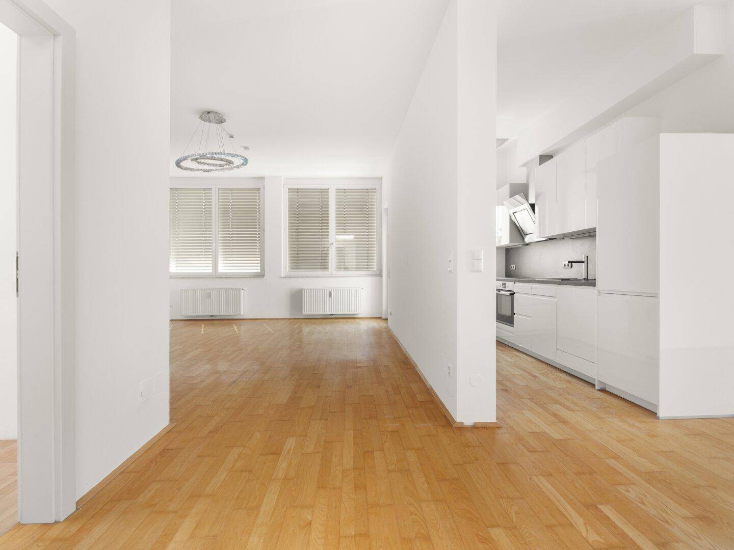 Offener Wohnbereich mit Parkettboden und moderner Küche im Hintergrund, ideal für geselliges Beisammensein.