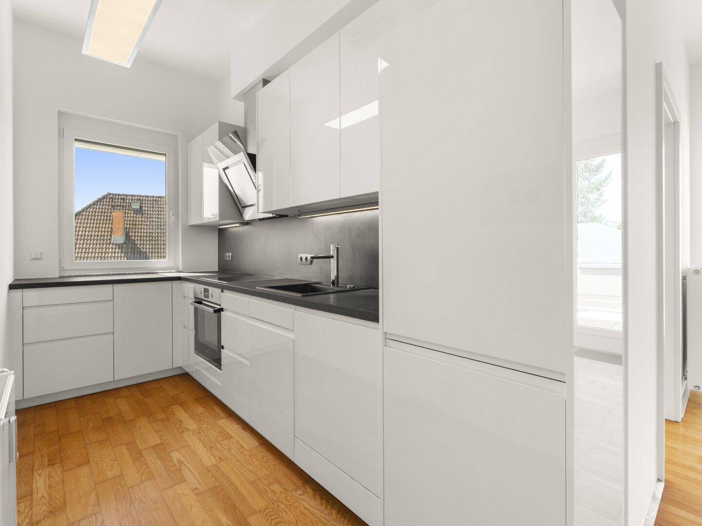 Moderne Einbauküche mit weißen Hochglanzfronten, dunkler Arbeitsplatte und Fenster.