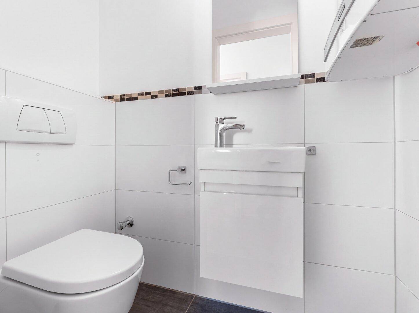 Separates Gäste-WC mit wandhängender Toilette und kleinem, modernem Waschbecken.