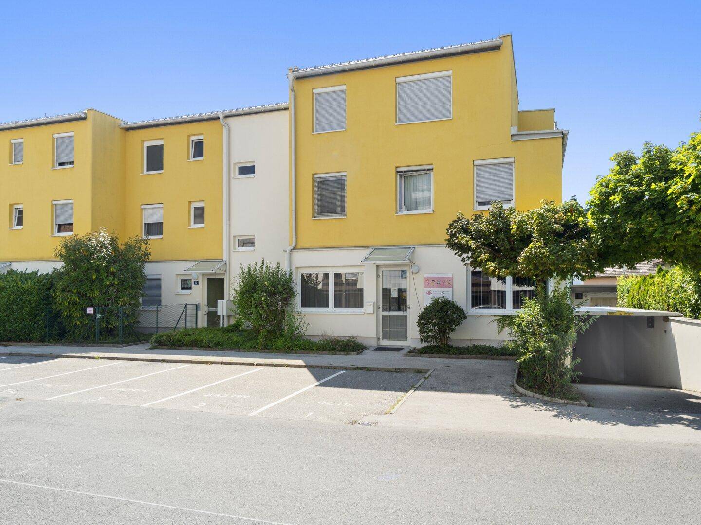 Mehrfamilienhaus mit auffälliger gelber Fassade und Parkplätzen im Vordergrund.