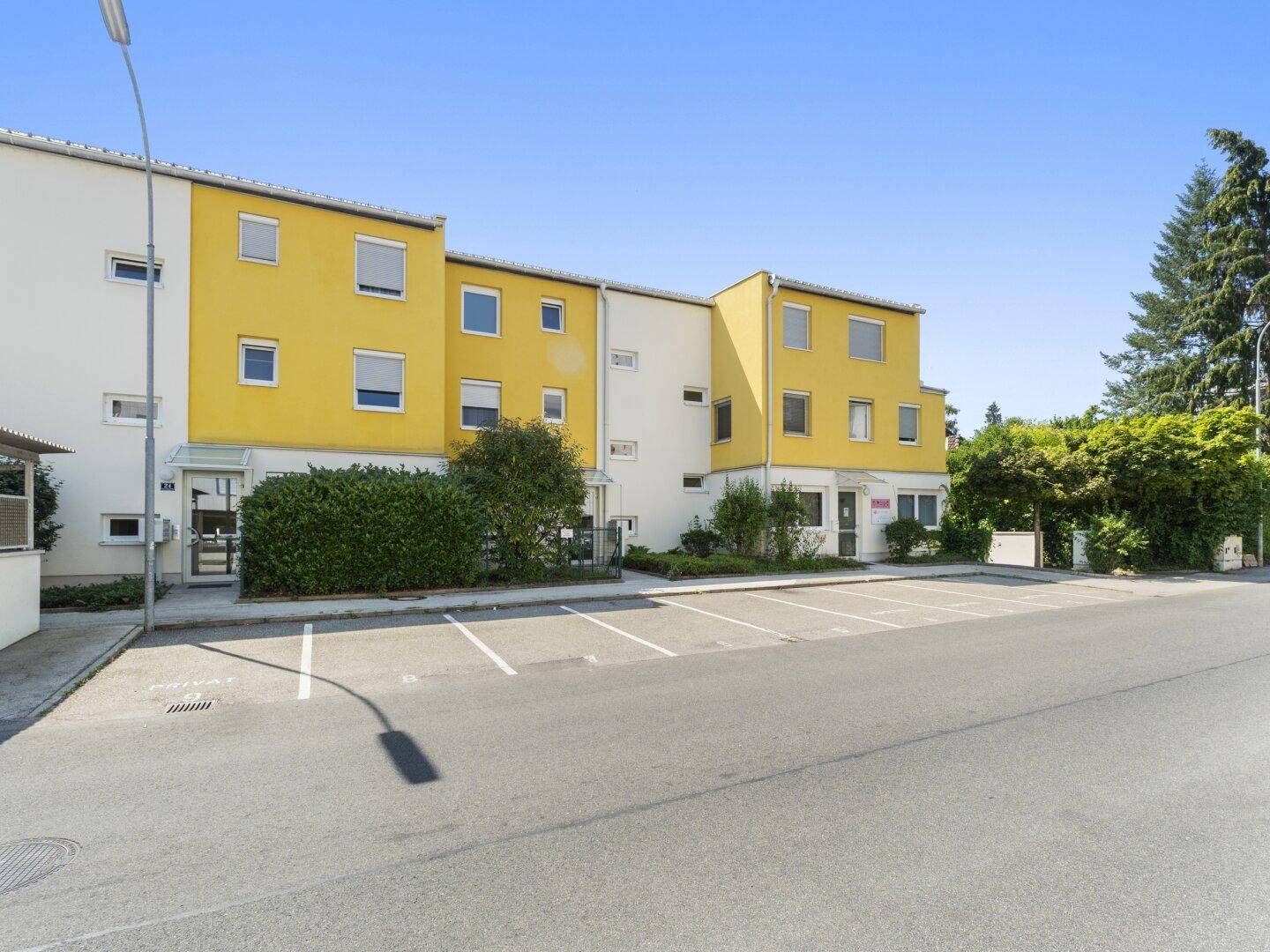 Modernes Wohngebäude mit gelber Fassade, umgeben von Grünflächen und Parkmöglichkeiten.