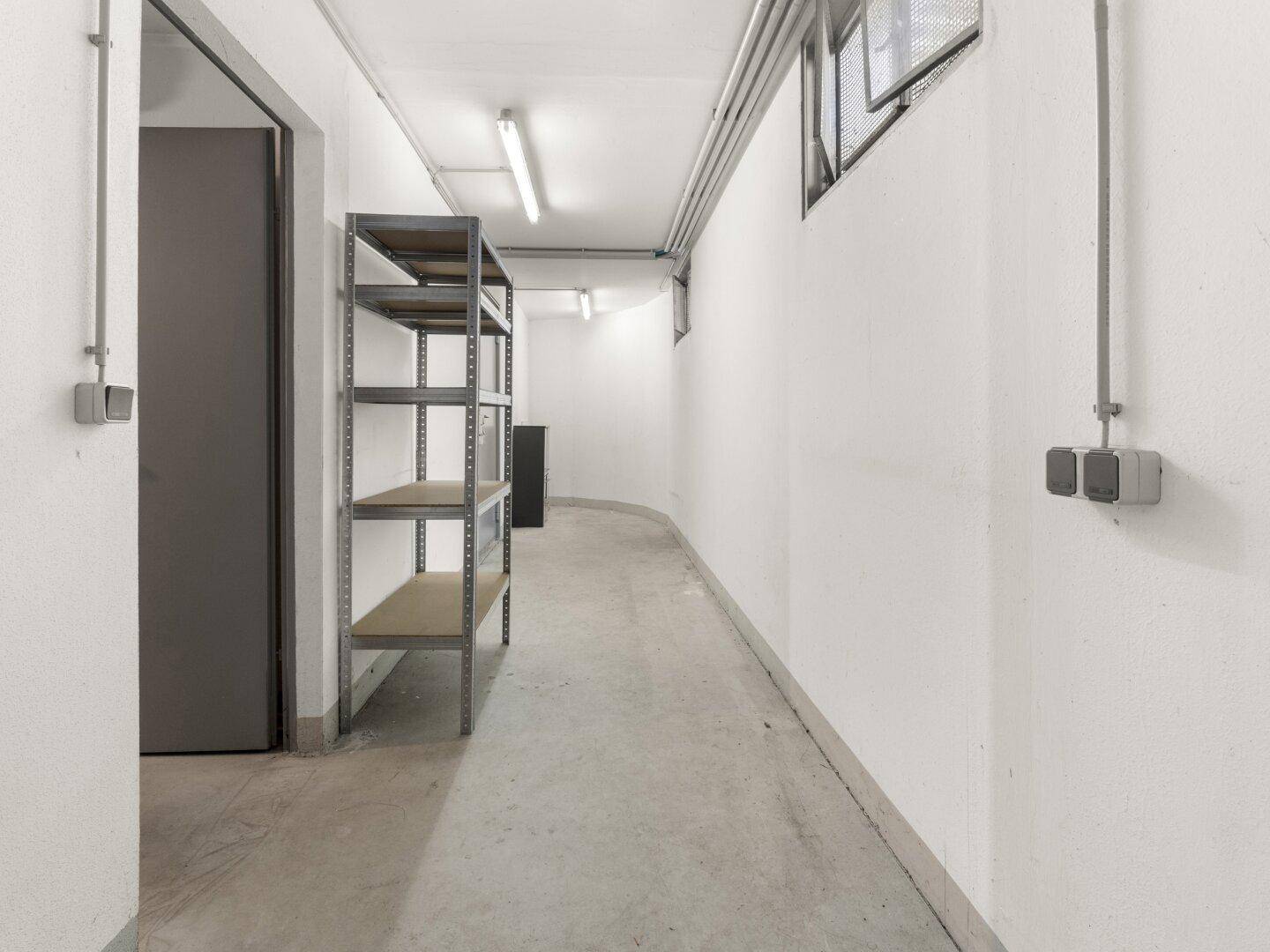 Geräumiger Kellerraum mit praktischen Regalen und einem strapazierfähigen Betonboden.