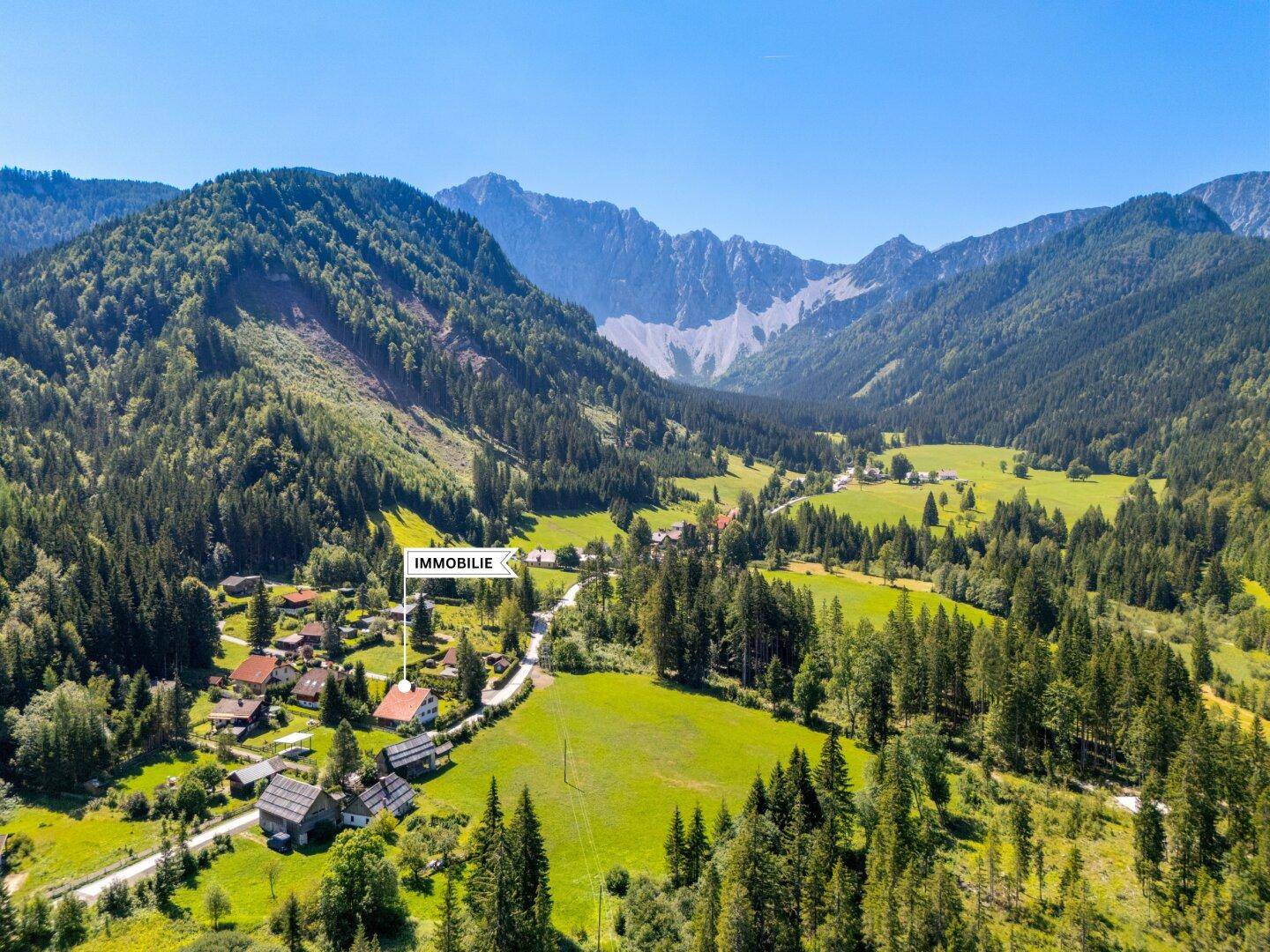 Weitläufige Luftaufnahme eines Hauses in einer idyllischen Berglandschaft mit weiten Wiesen.