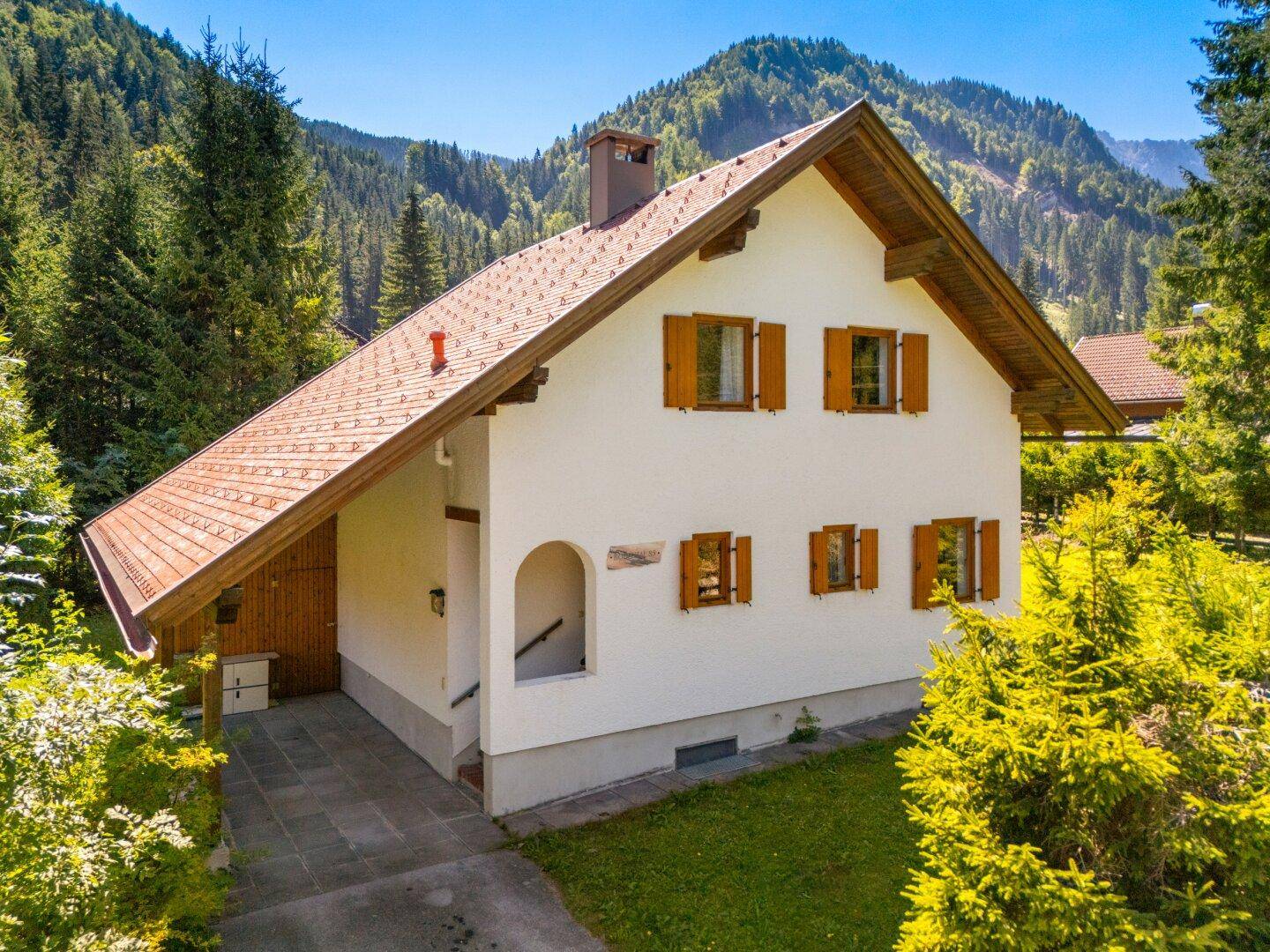 Charmantes Haus mit weißer Fassade, Holzfensterläden und Satteldach in alpiner Umgebung.