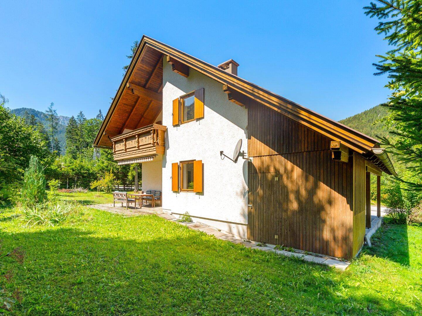 Seitenansicht des Hauses mit großem Rasenbereich und Blick auf die umliegenden Wälder.
