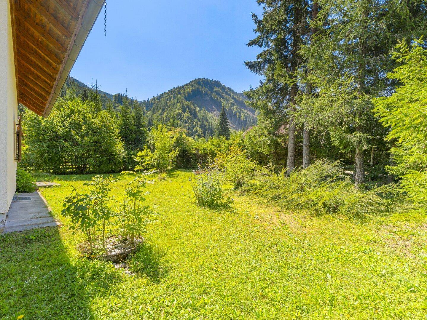 Gepflegter Gartenbereich neben dem Haus mit Blick auf bewaldete Hügel.