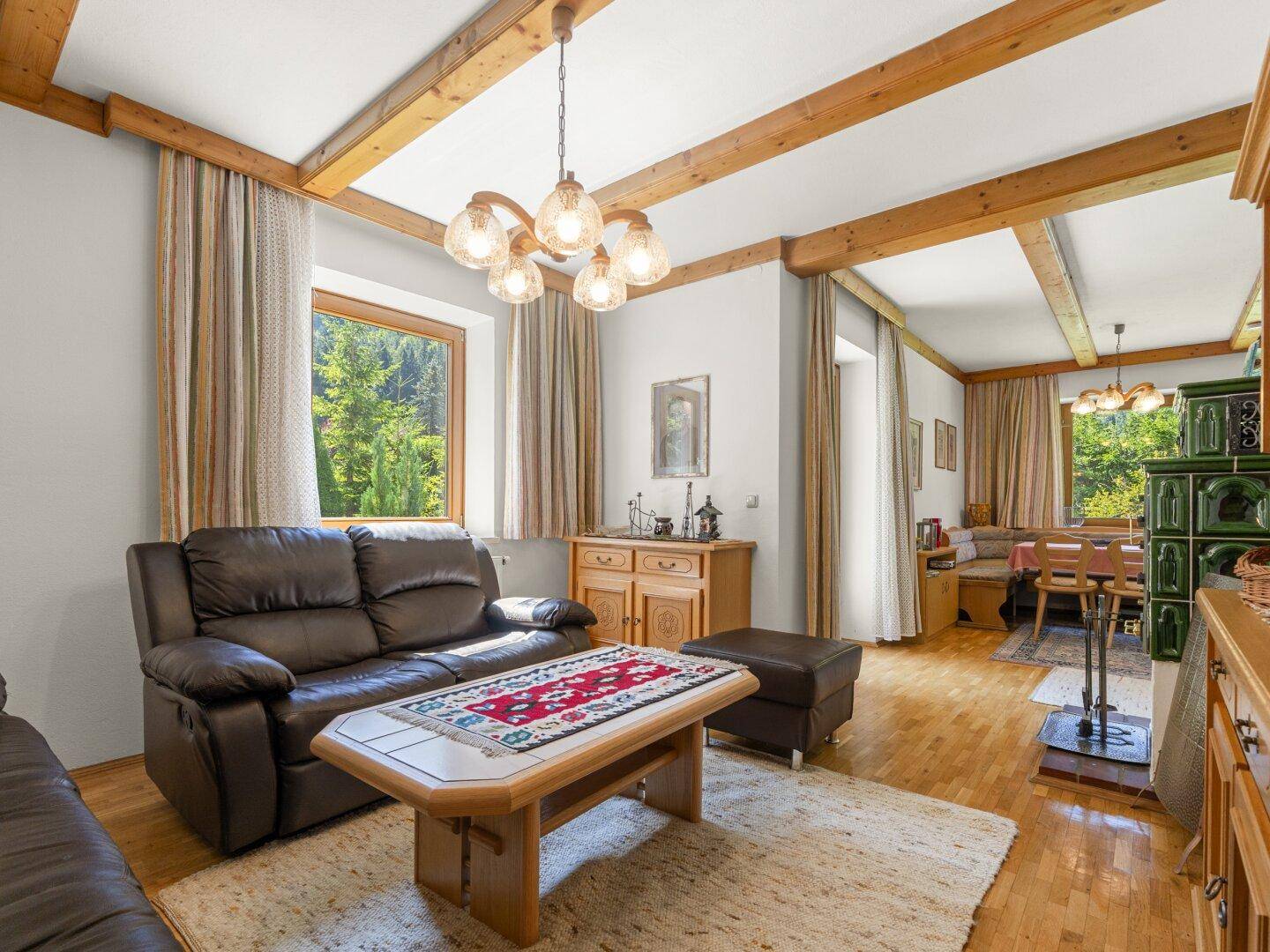 Traditioneller Wohnbereich mit Holzbalkendecke, Kachelofen und Blick ins Grüne.