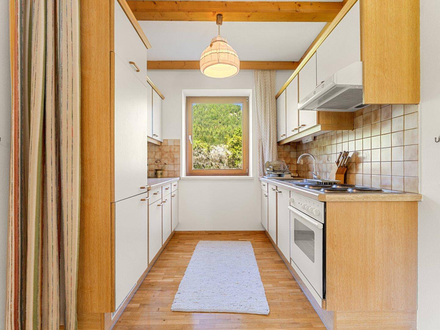 Kleine, funktionale Küche mit Holz- und weißen Schränken und Fensterblick ins Grüne.