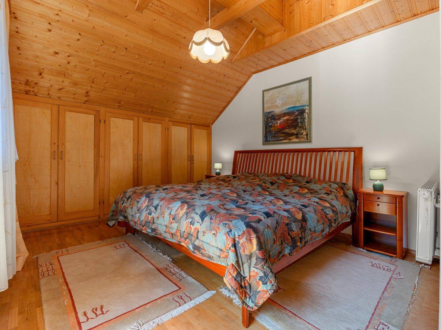 Geräumiges Schlafzimmer mit Holzbalkendecke, Einbauschränken und Doppelbett.